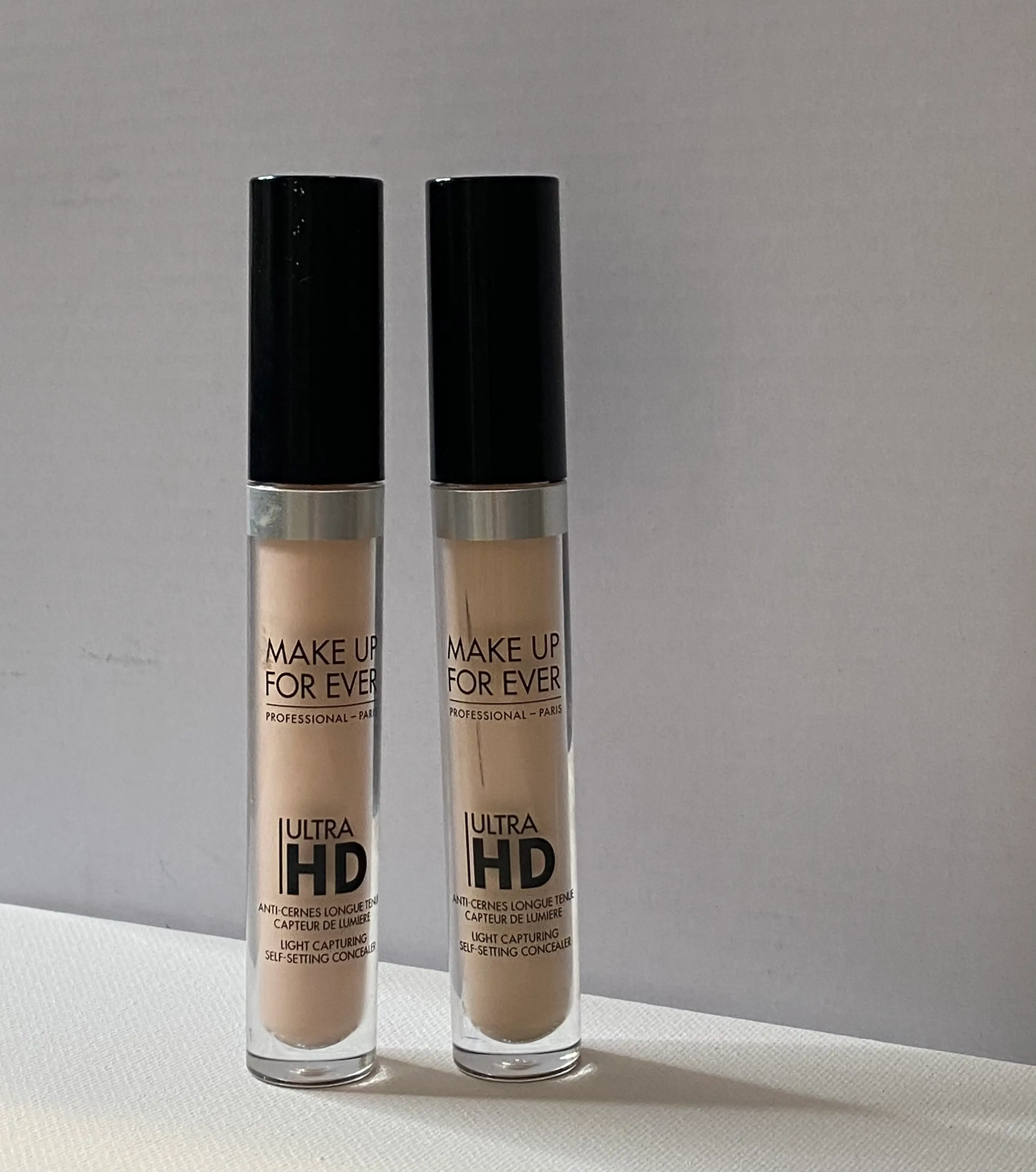 Two light-colored concealers with black caps and bold text with 