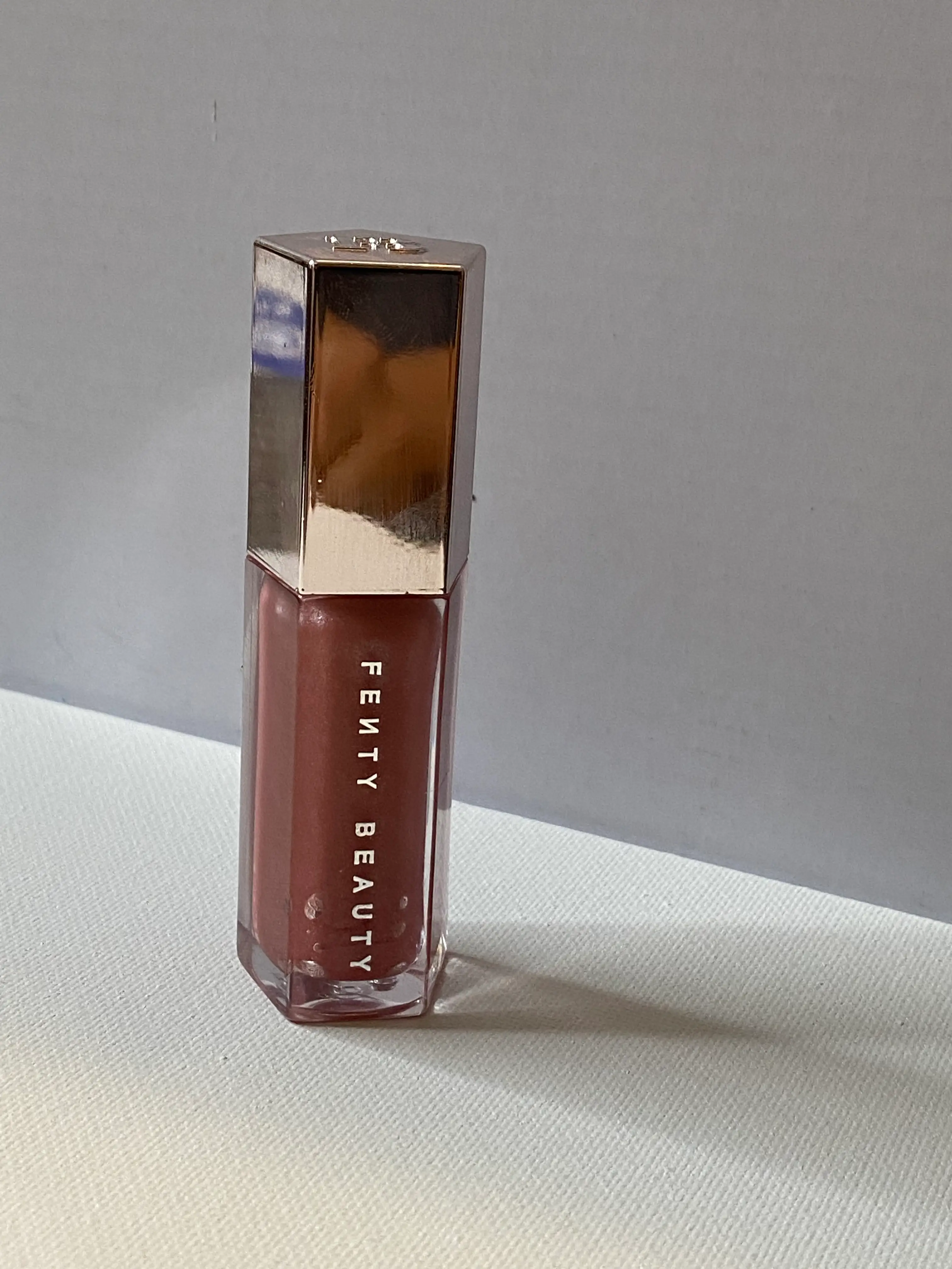 A pentagon-shaped tube of light pink lip gloss with 