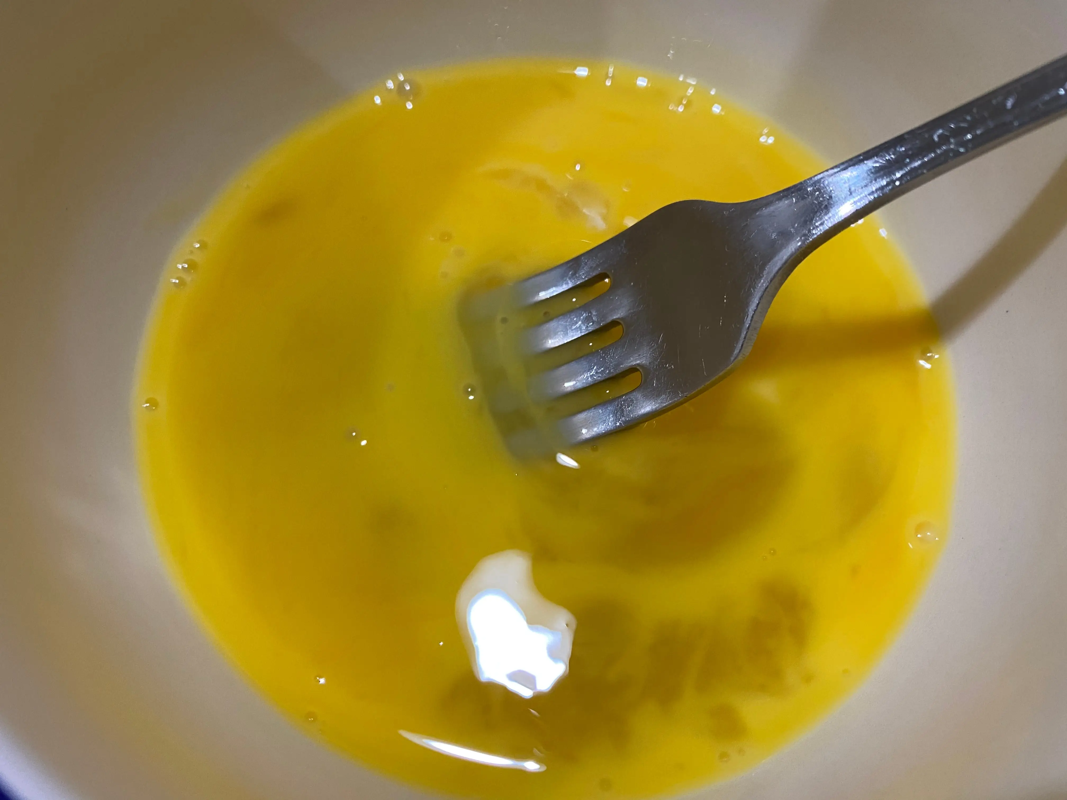 Raw eggs mixed with a fork in a white bowl