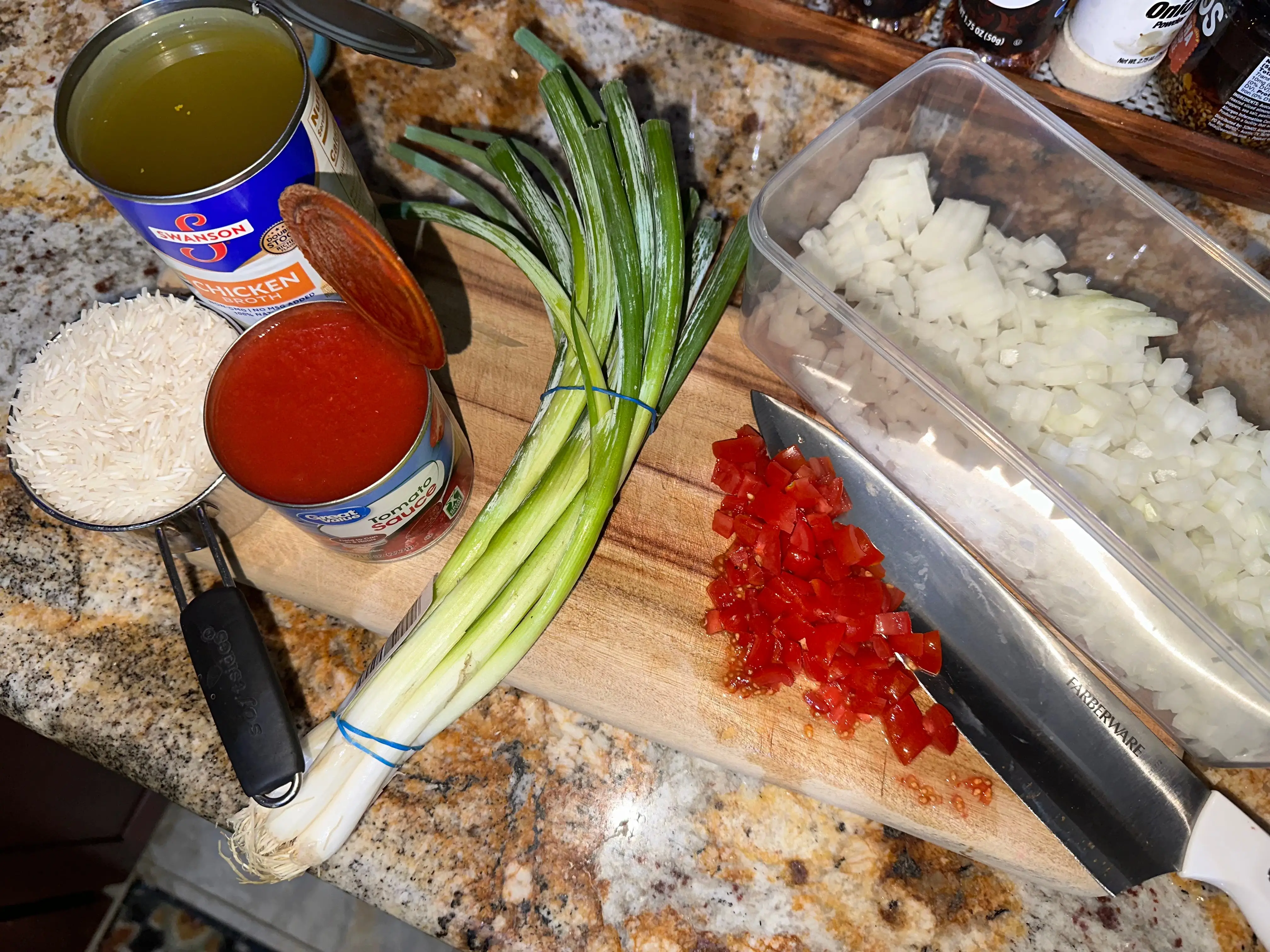 Taco night ingredients, tomatoes, onions, rice, a knife, and cutting board.