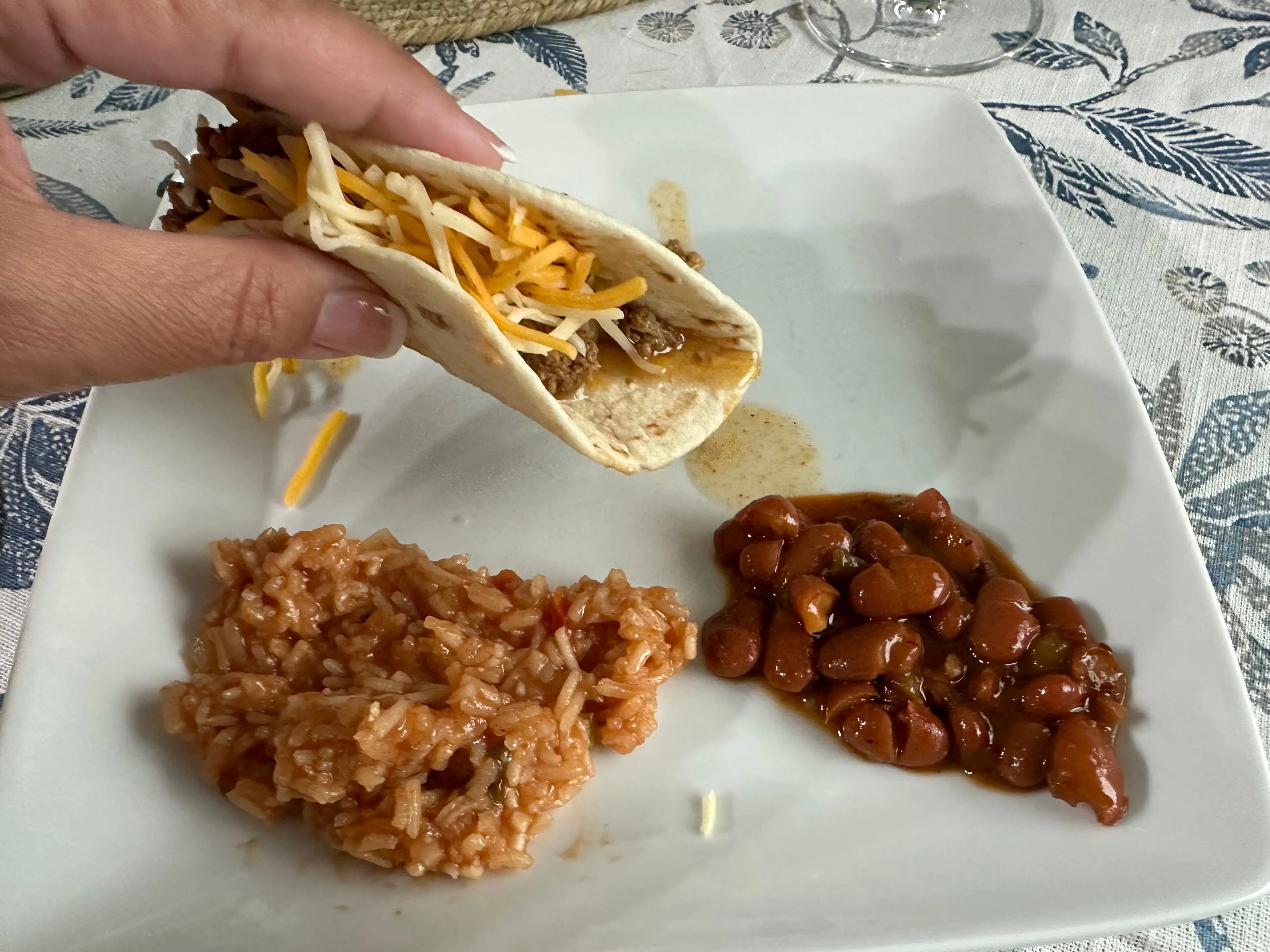 Hand holding a taco over a plate with beans and Mexican rice.