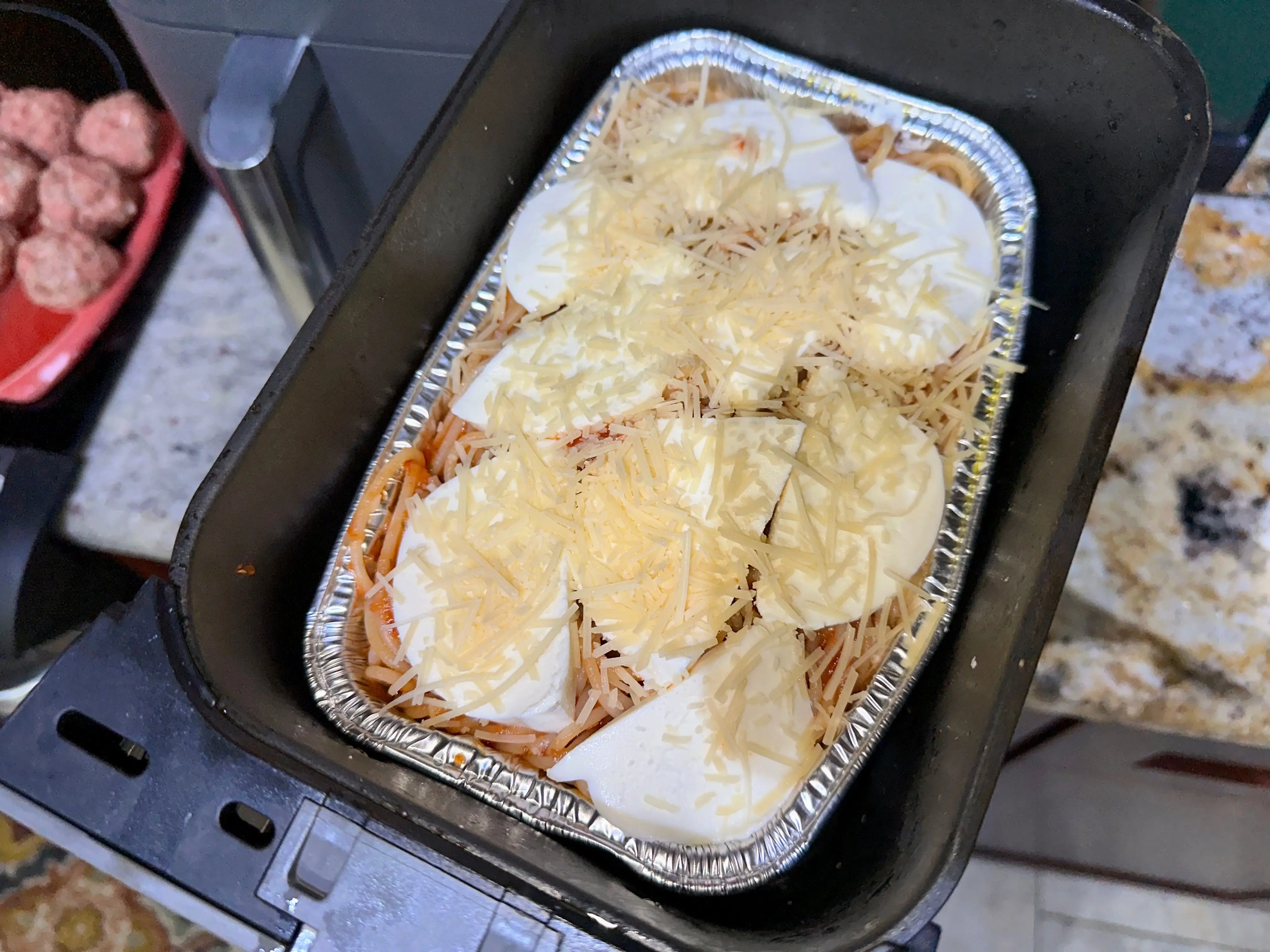 Spaghetti with sauce and cheese in a foil pan, placed in an air-fryer basket.