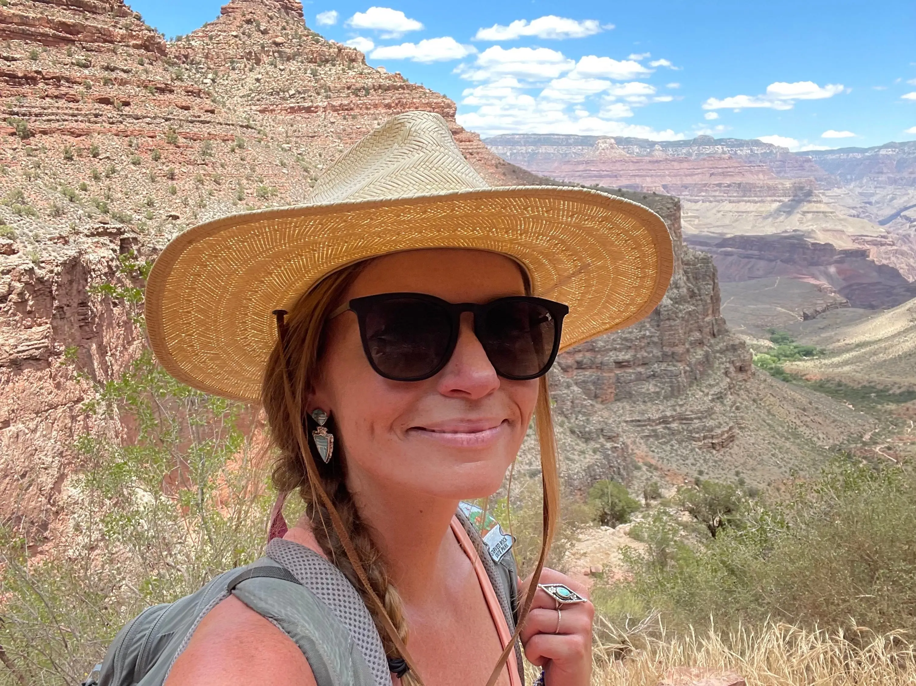 A woman with a straw hat, backpack, and sunglasses at the Grand Canyon.