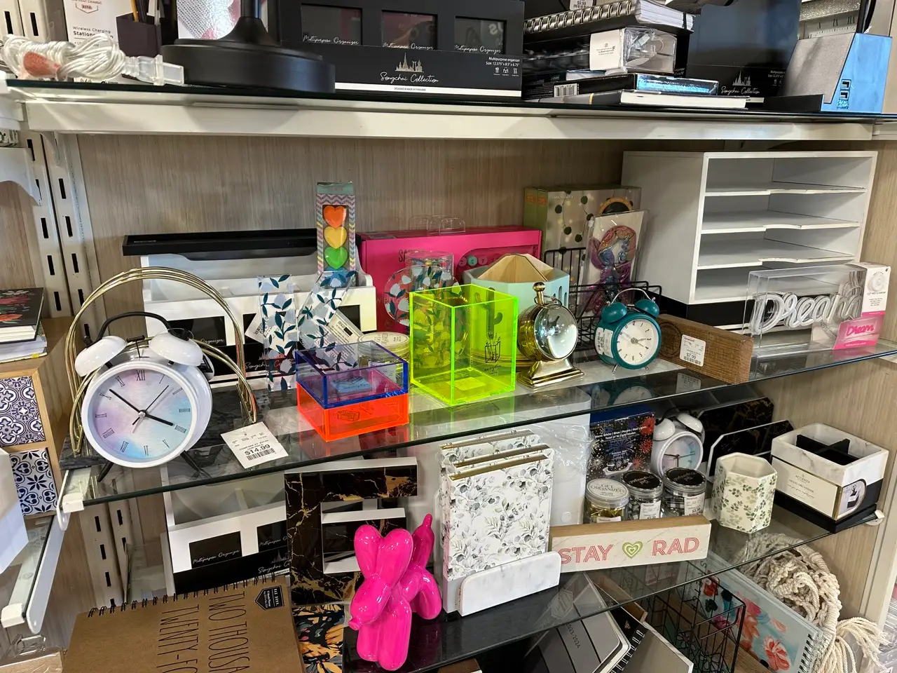 Office-supplies section in a HomeGoods store with neon-yellow pencil organizers, small alarm clocks, paperweights, and other small desk items