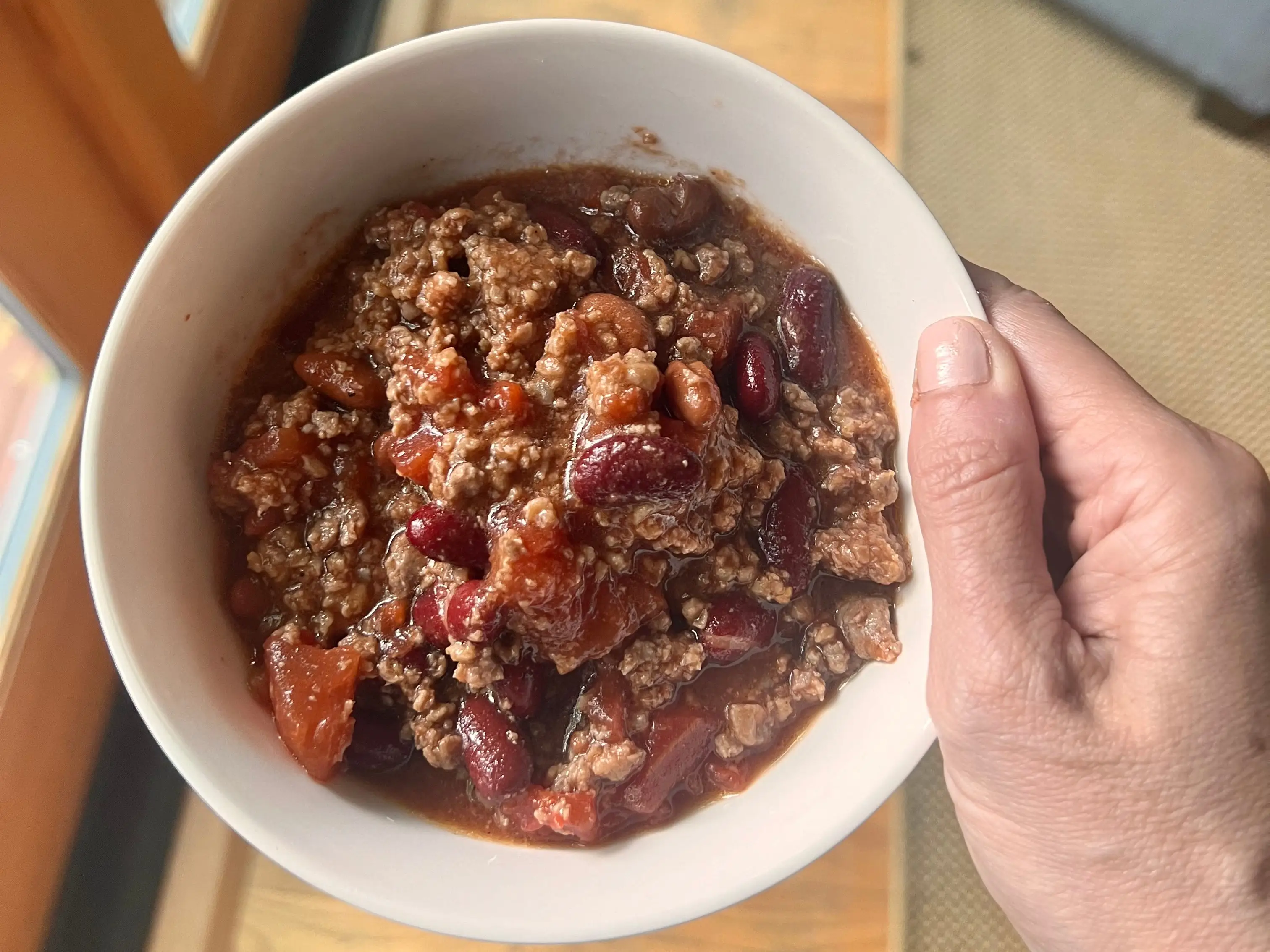 hand holding up a bowl of meat and bean chili