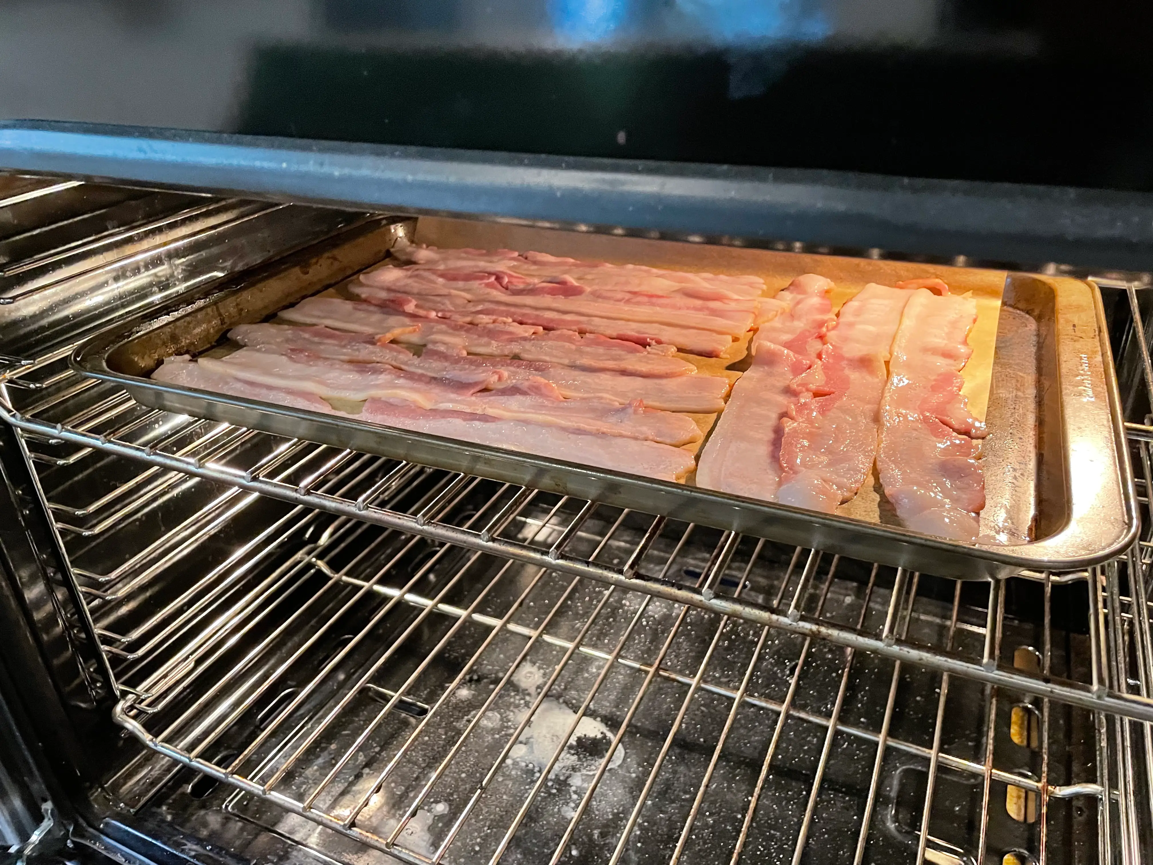 a sheet pan of bacon on parchment paper in an oven