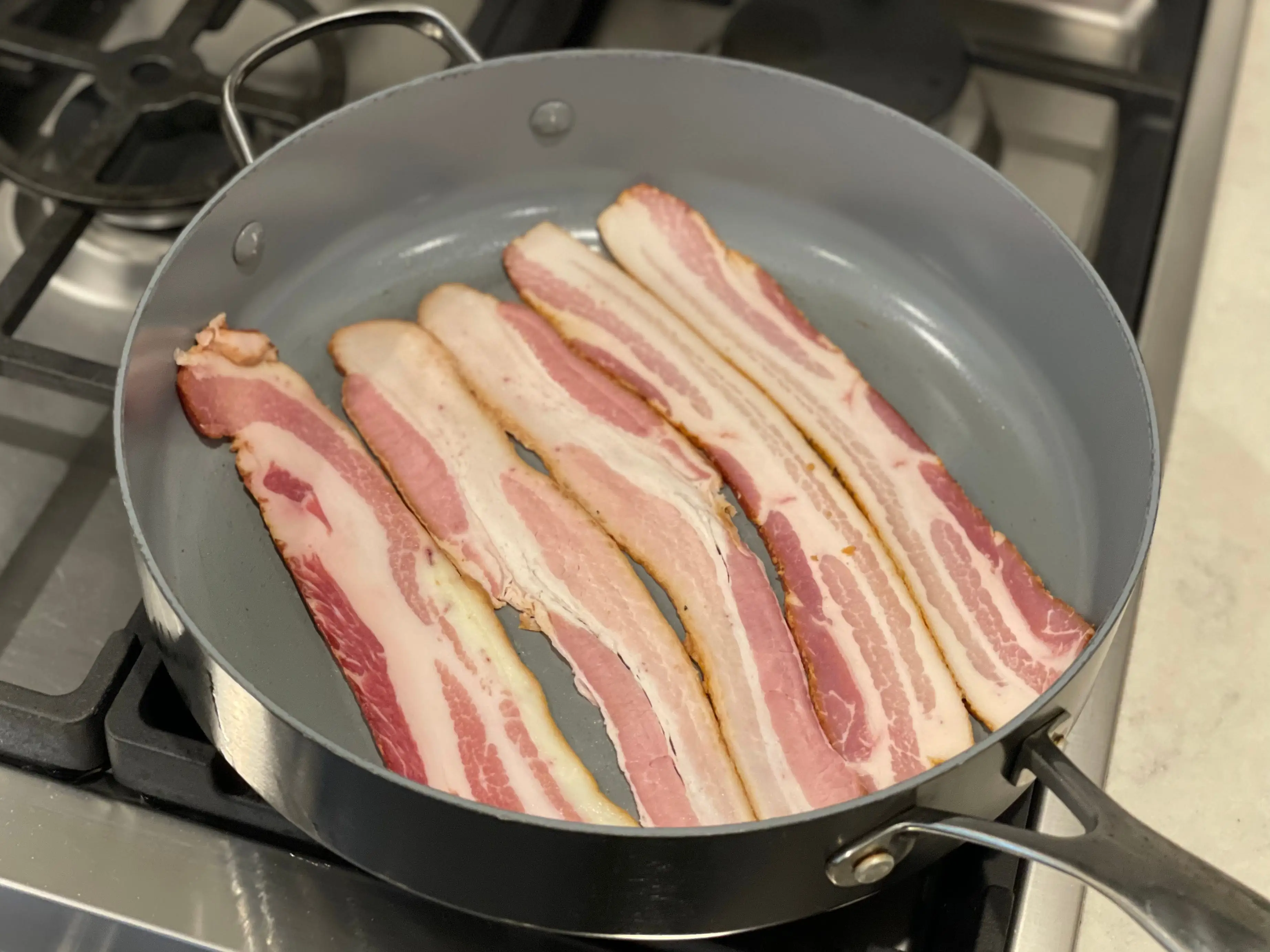 raw strips of bacon in a frying pan