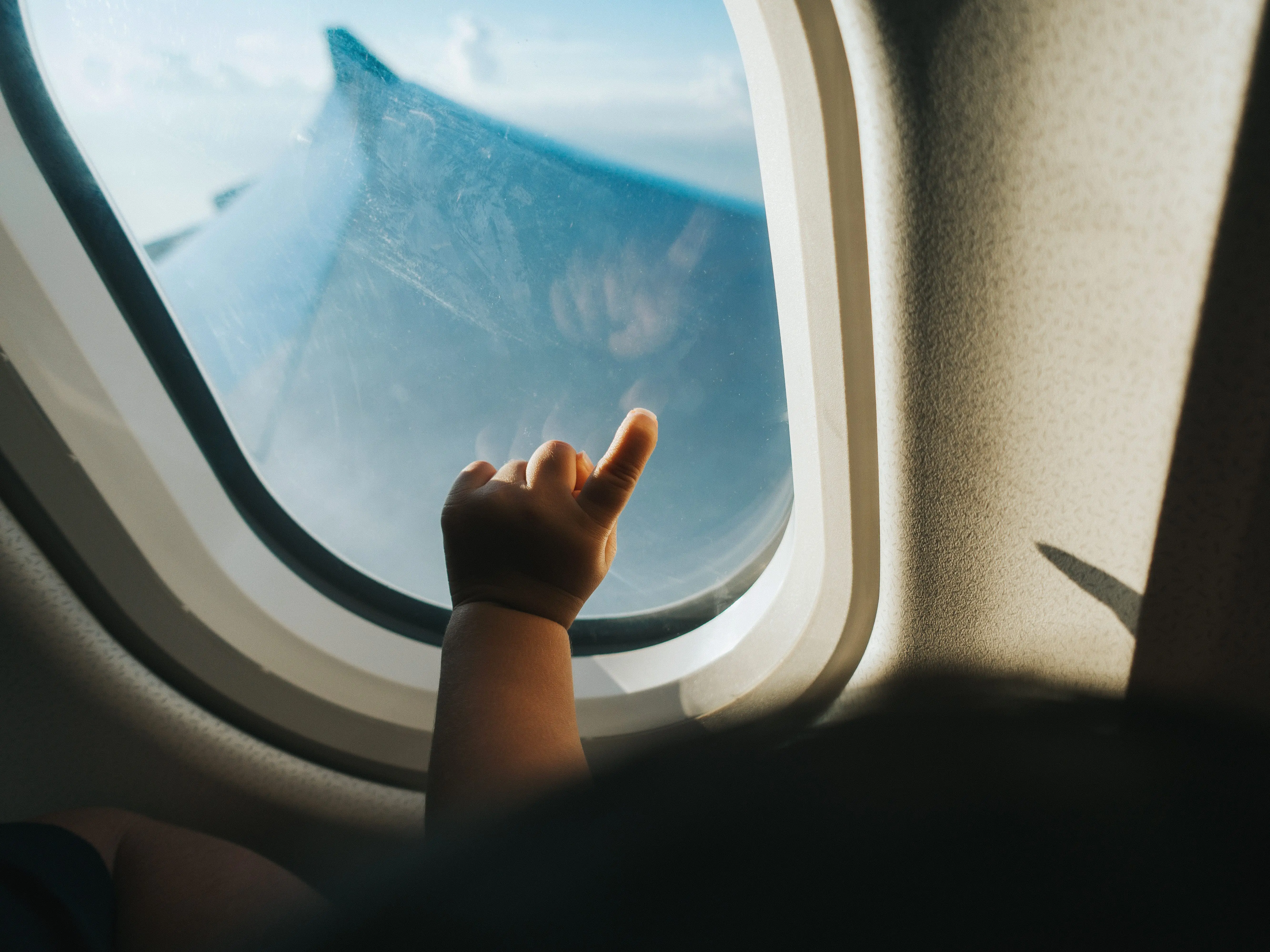 A toddler's hand points against the window of an airplane.
