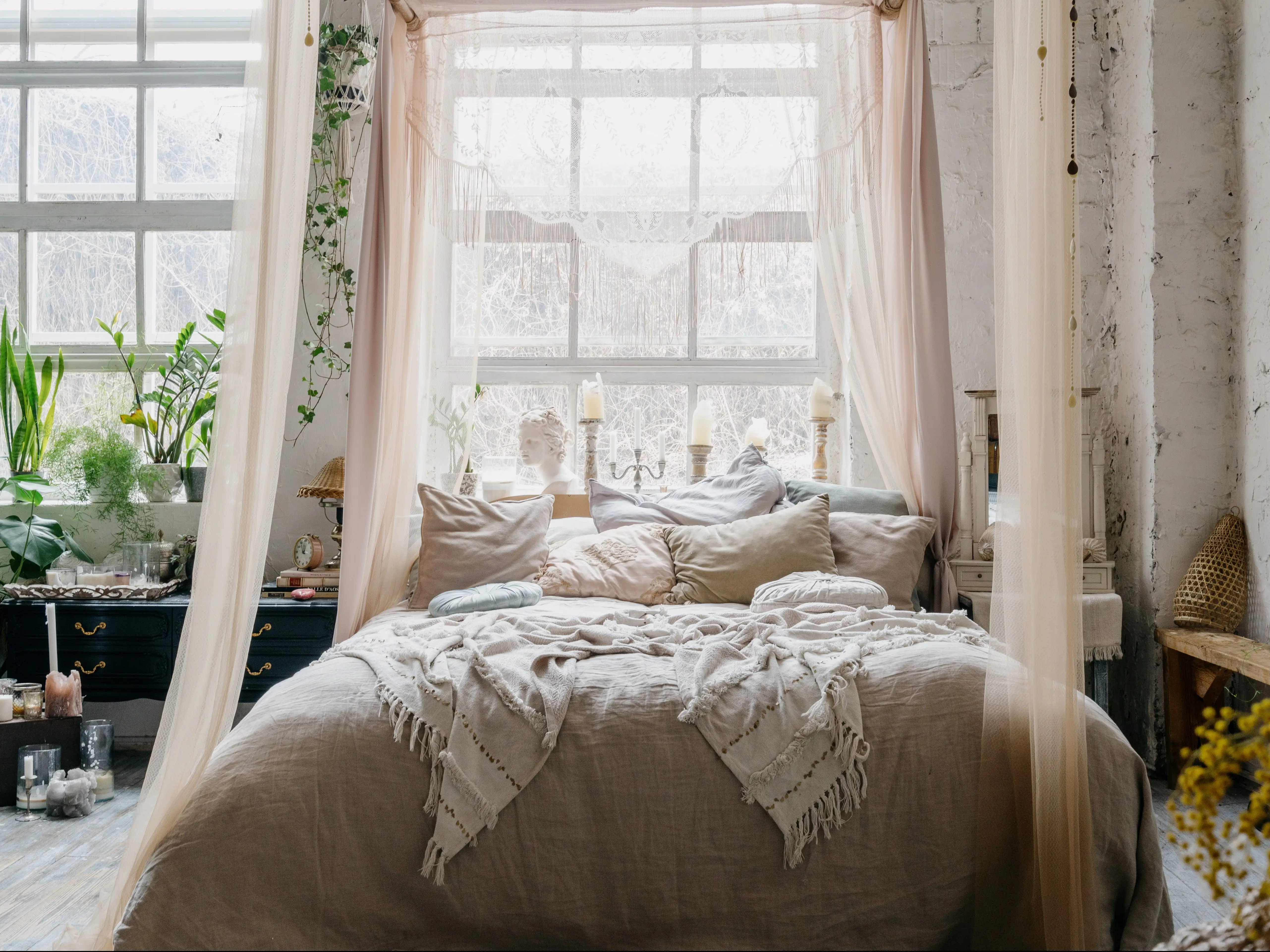 A bedroom featuring a canopy bed with neutral-colored bedding and plants throughout the room.