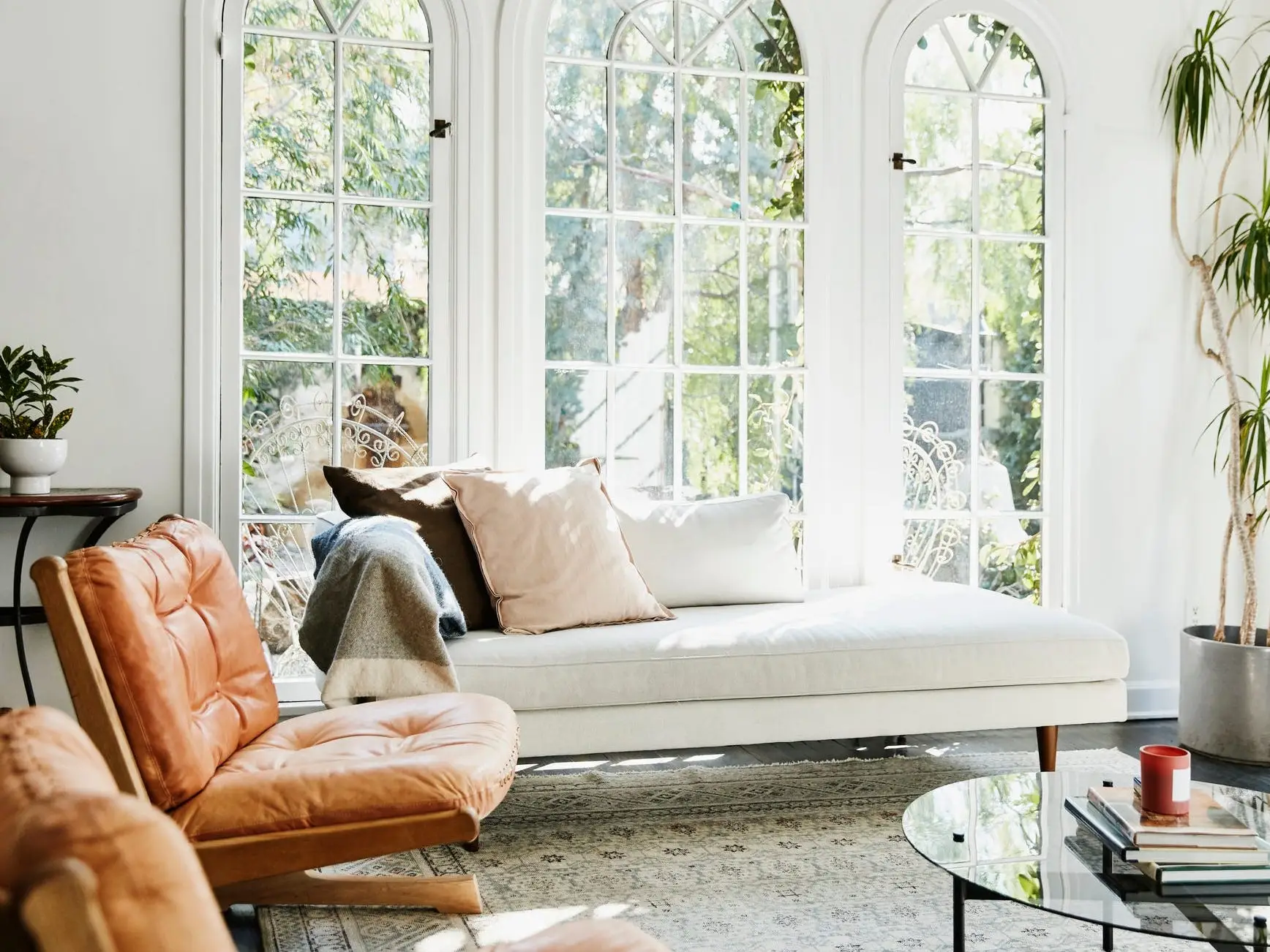A white couch sitting in front of a room with three large arched windows. An orange chair sits to the left of the white couch.