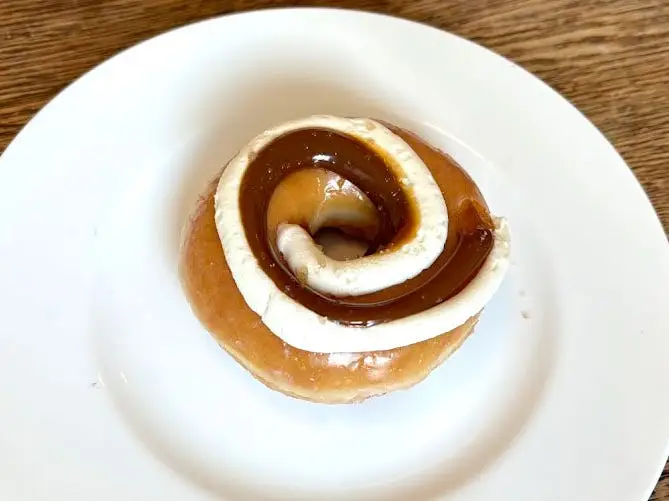 A glazed doughnut topped with swirls of brown and white frosting on a white plate.