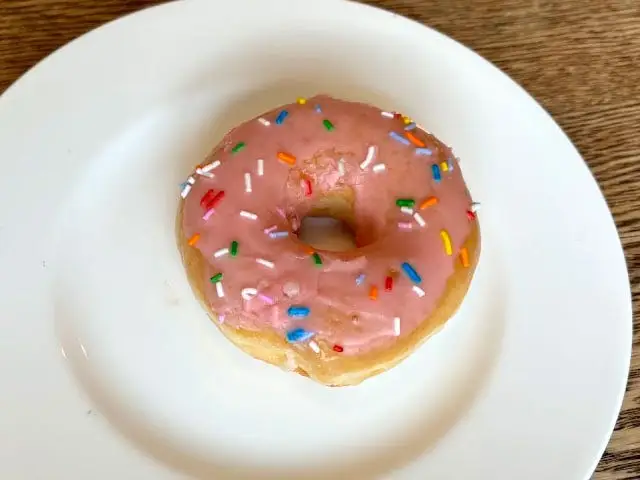 A doughnut topped with pink icing and colorful sprinkles on a white plate.