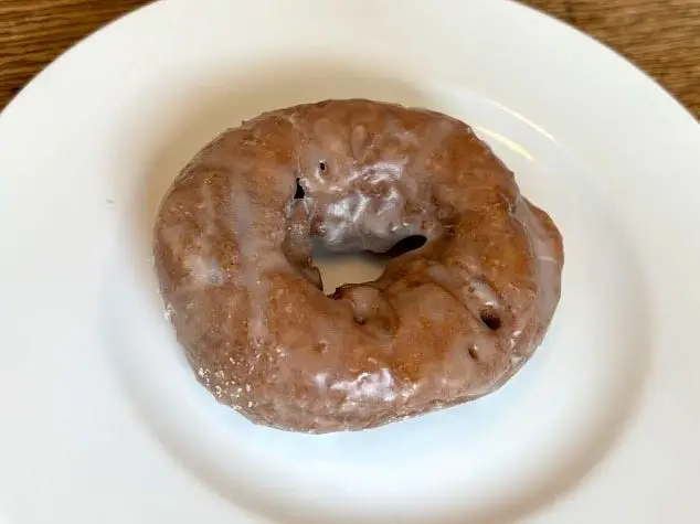A dark-colored glazed doughnut on a white plate.