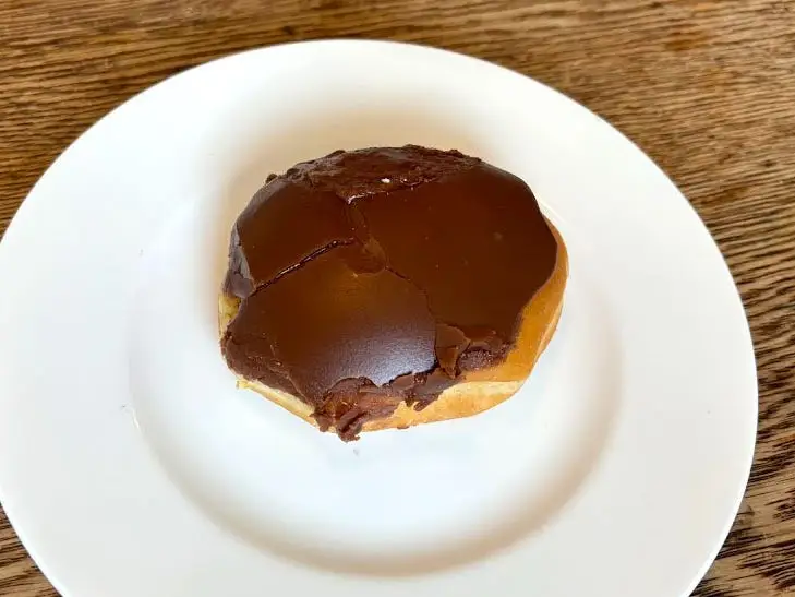 A doughnut with no hole that's topped with chocolate icing on a white plate.