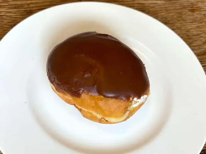 A doughnut with no hole that's topped with chocolate icing on a white plate.