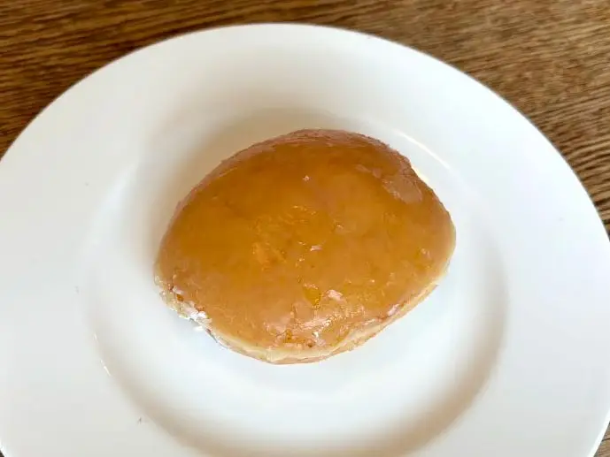 A glazed doughnut with no hole on a white plate.