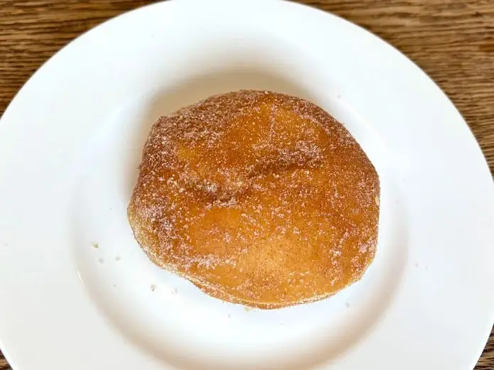 A doughnut with no hole that's topped with granulated sugar on a white plate.