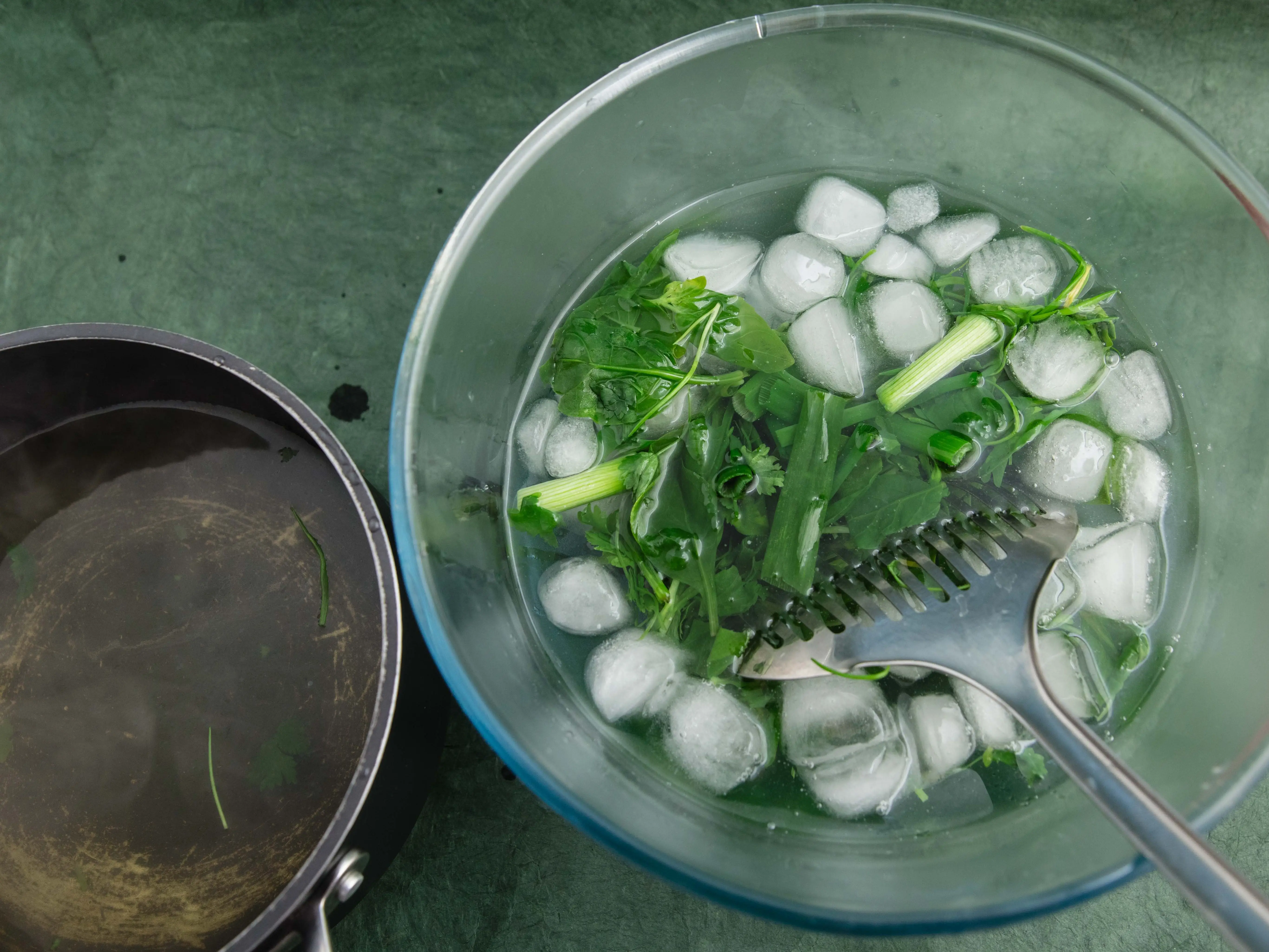 Ice-water bath with greens in it being moved by metal spoon