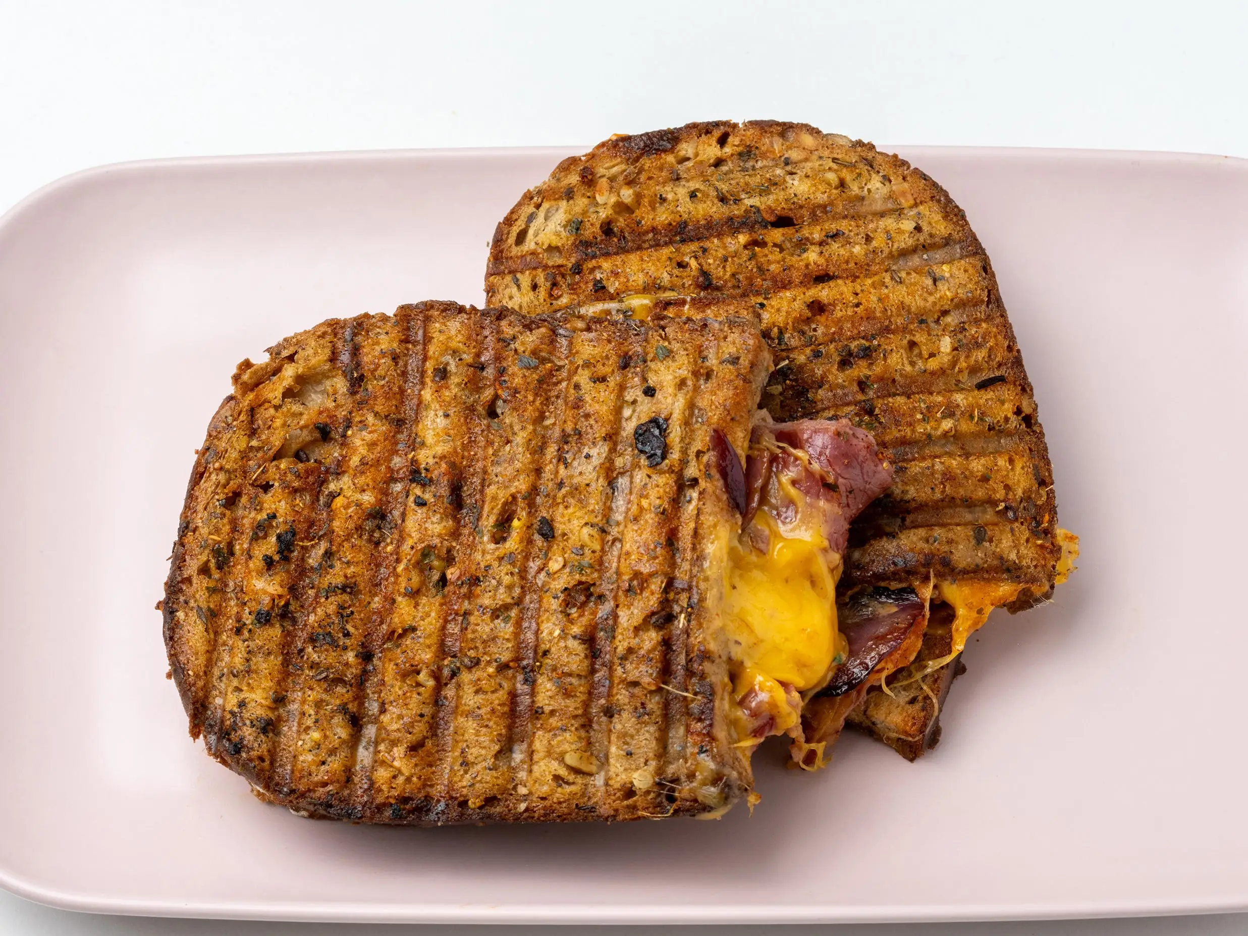 Grilled cheese on rounded bread with bacon and cheese oozing out on pink plate