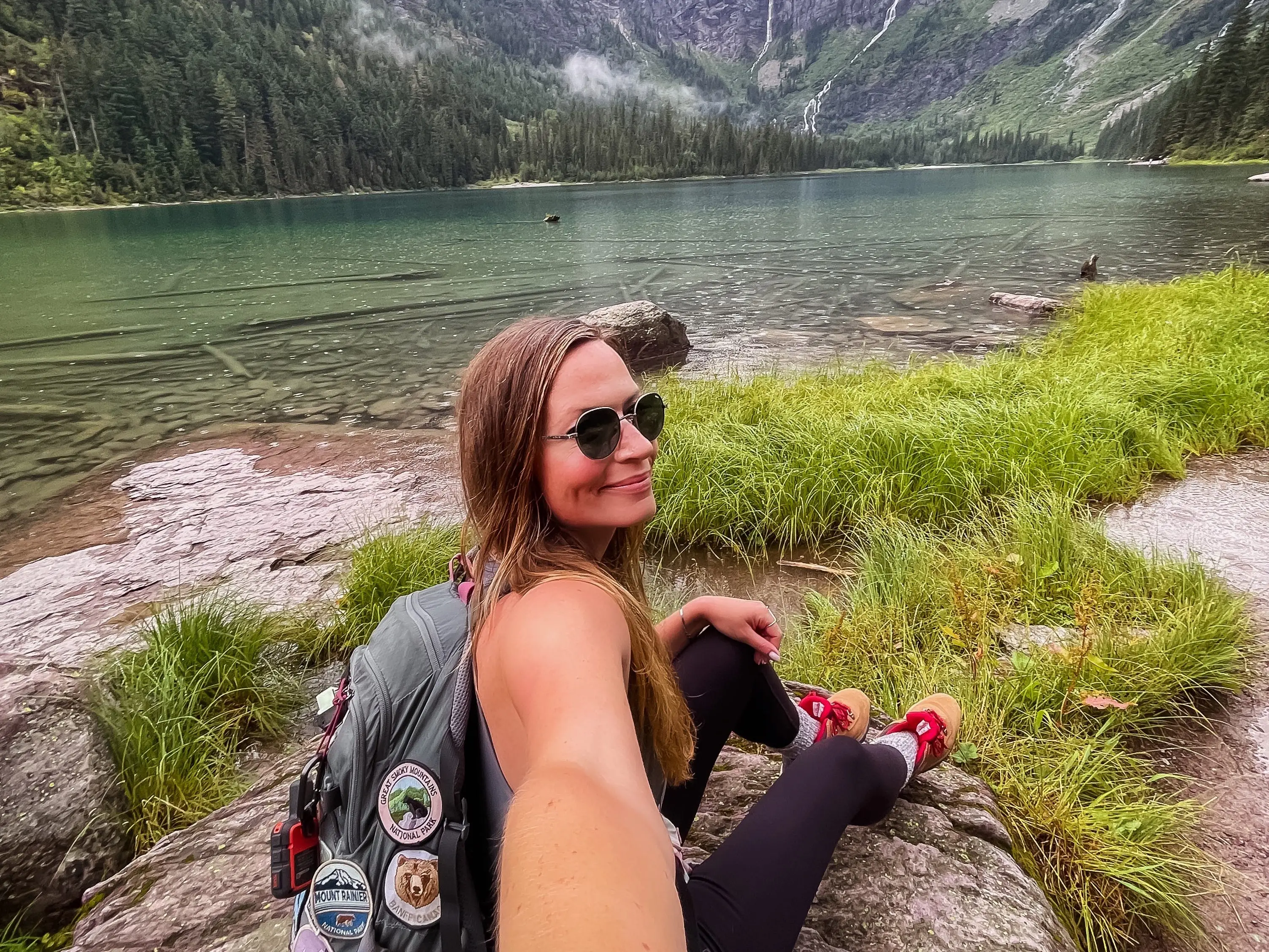 A woman taking a selfie in front of a lake and mountains.