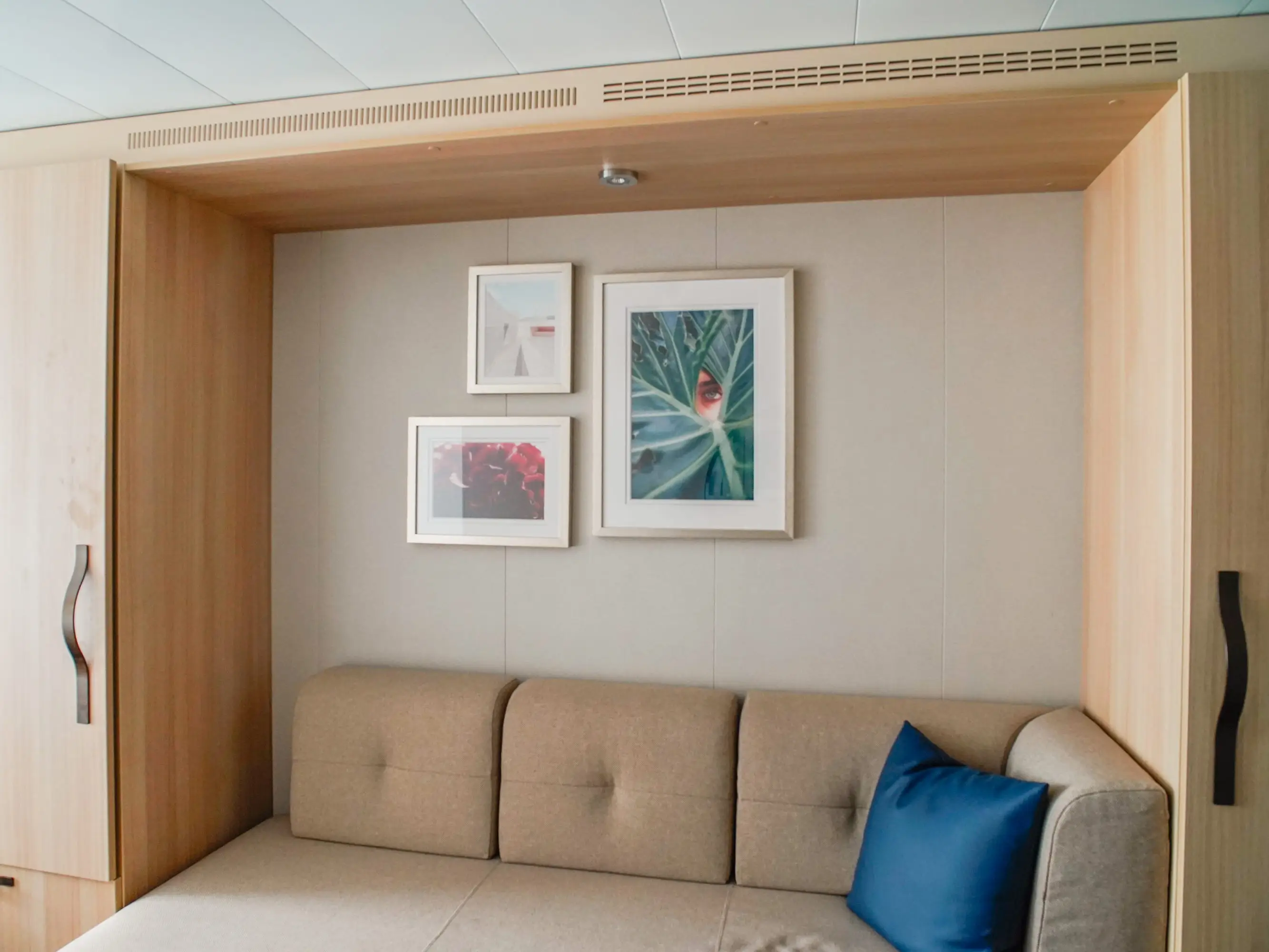 A beige couch surrounded by a built-in closet in a cruise ship cabin