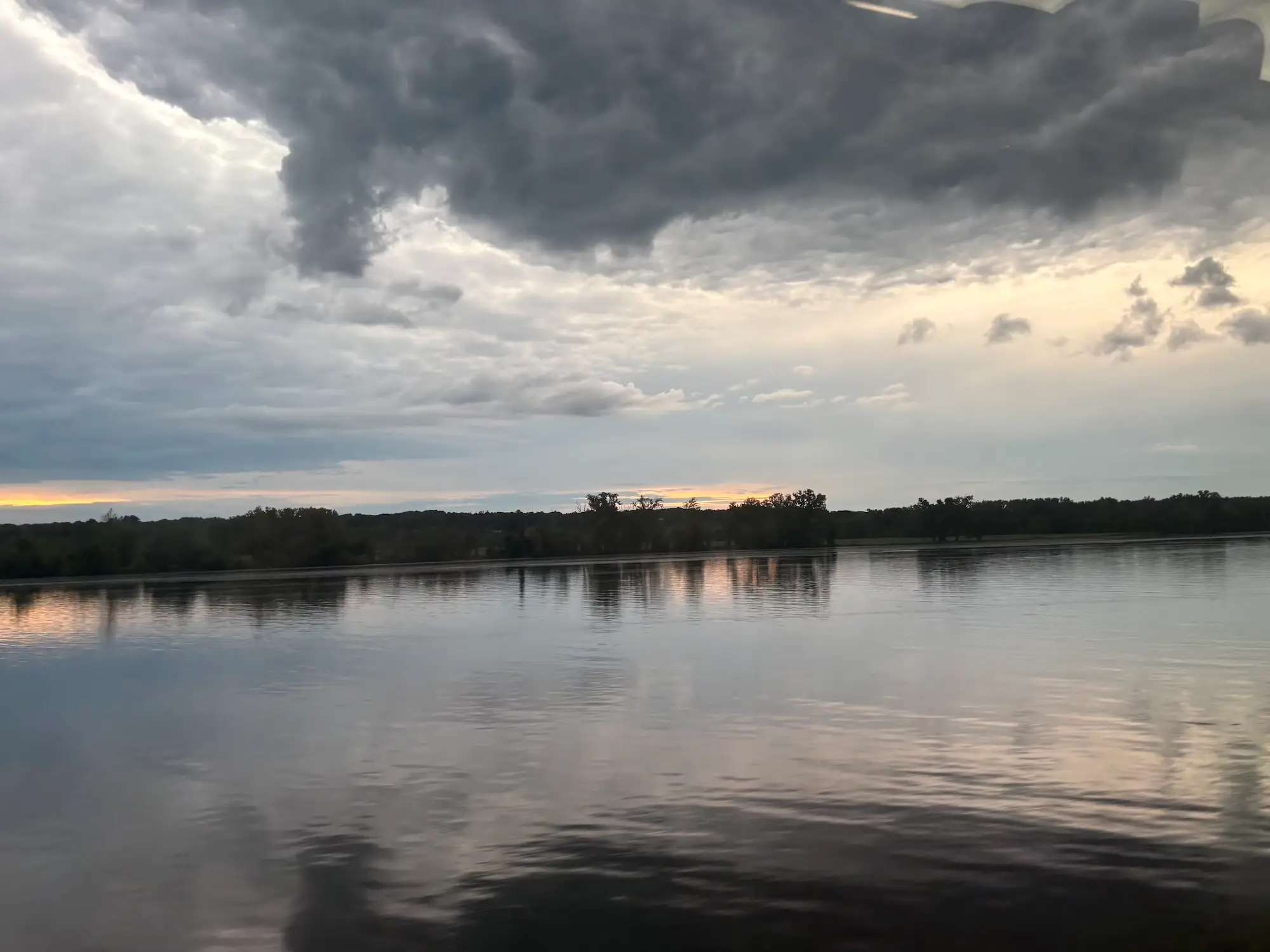 A lake surrounded by trees with clouds in the sky.