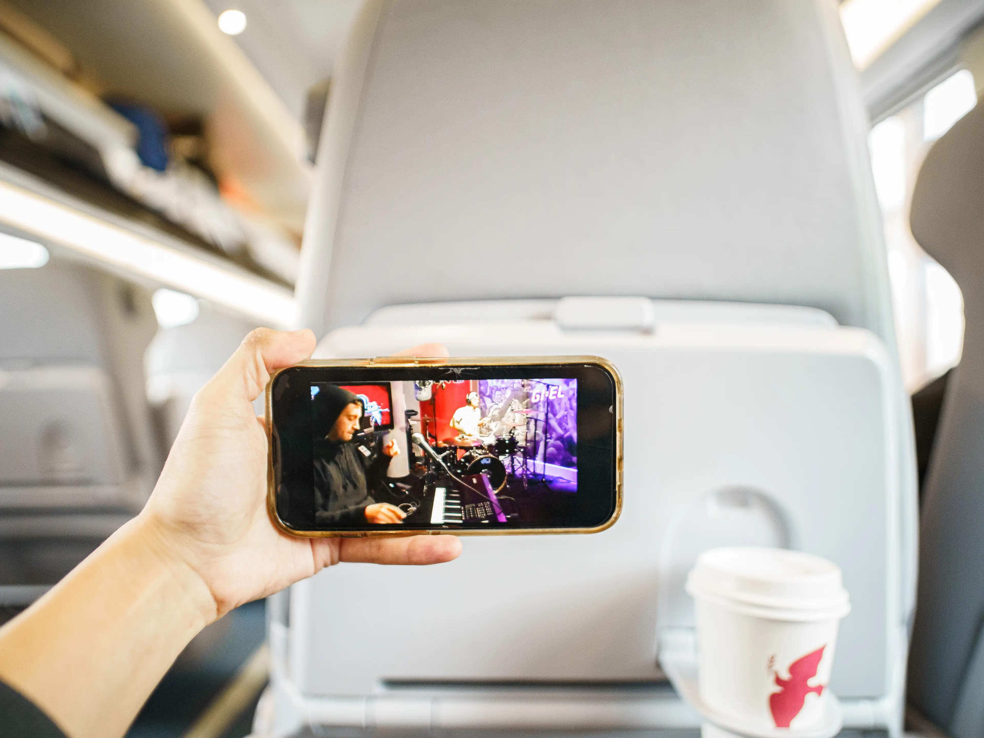 A hand holds a phone playing a music video in front of a train seat back