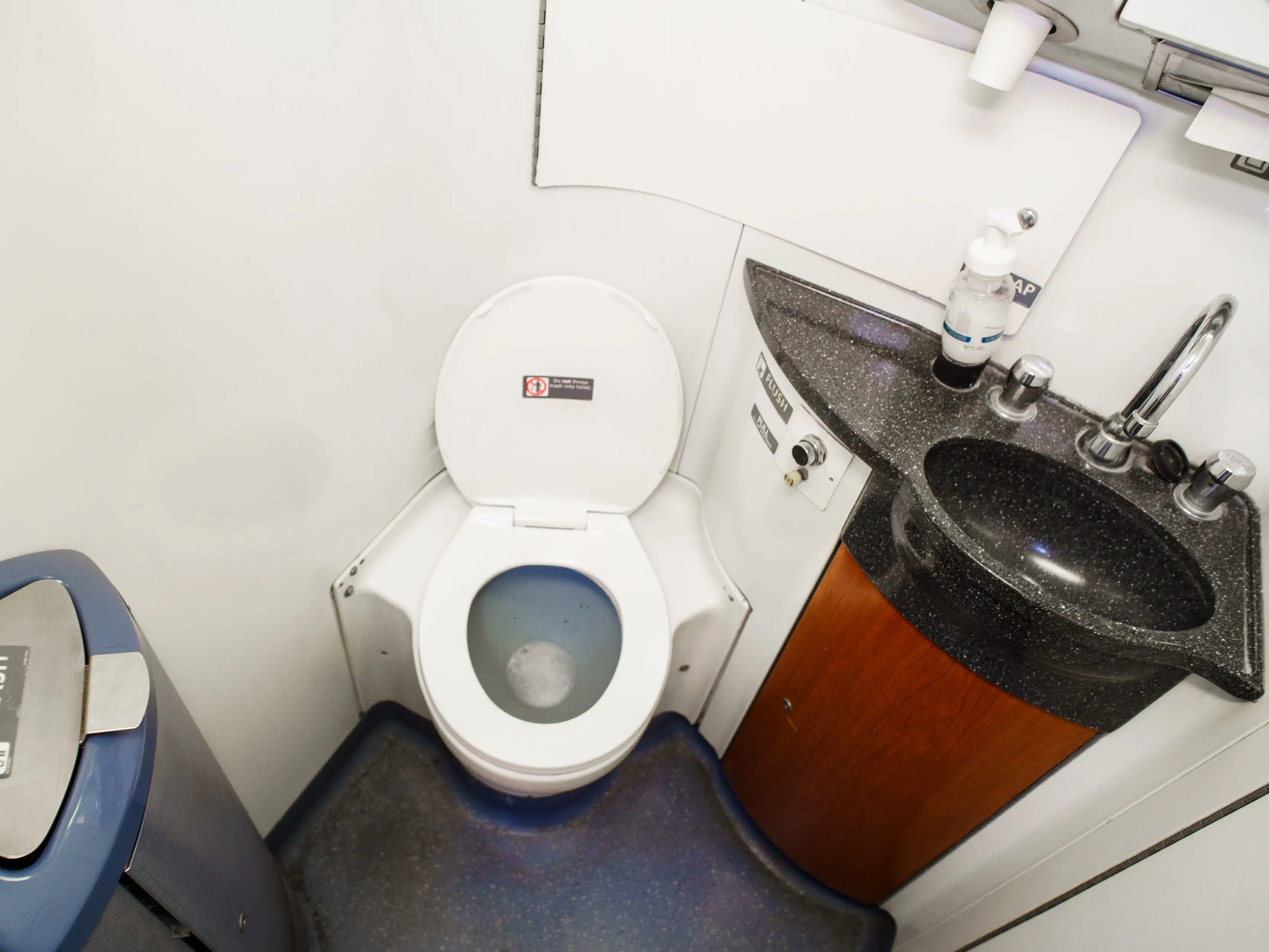 Inside a bathroom on an Amtrak train with a trash can on the left, a sink on the right, and a toilet in the middle