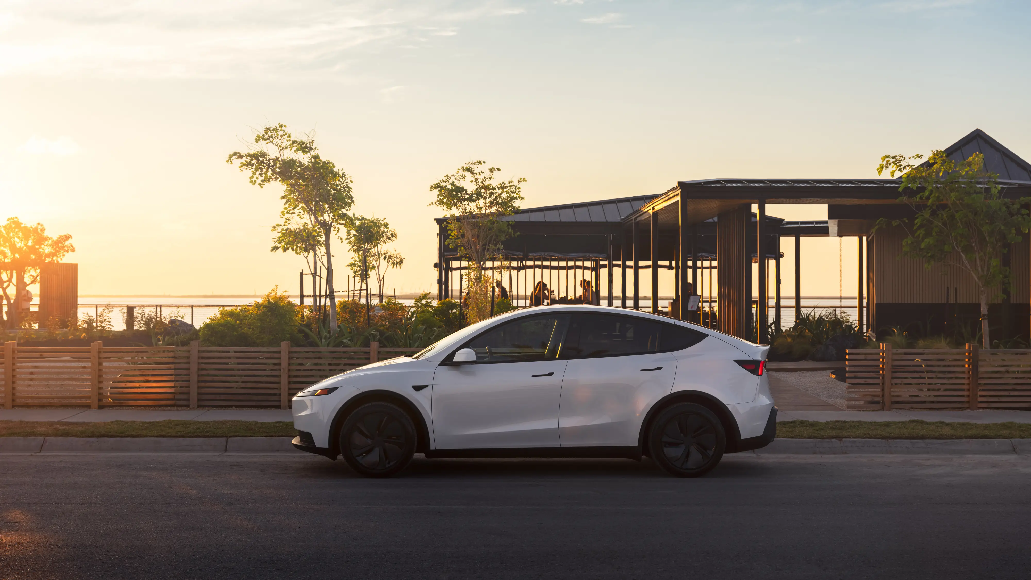 A white Tesla Model Y Standard is parked next to a small park.