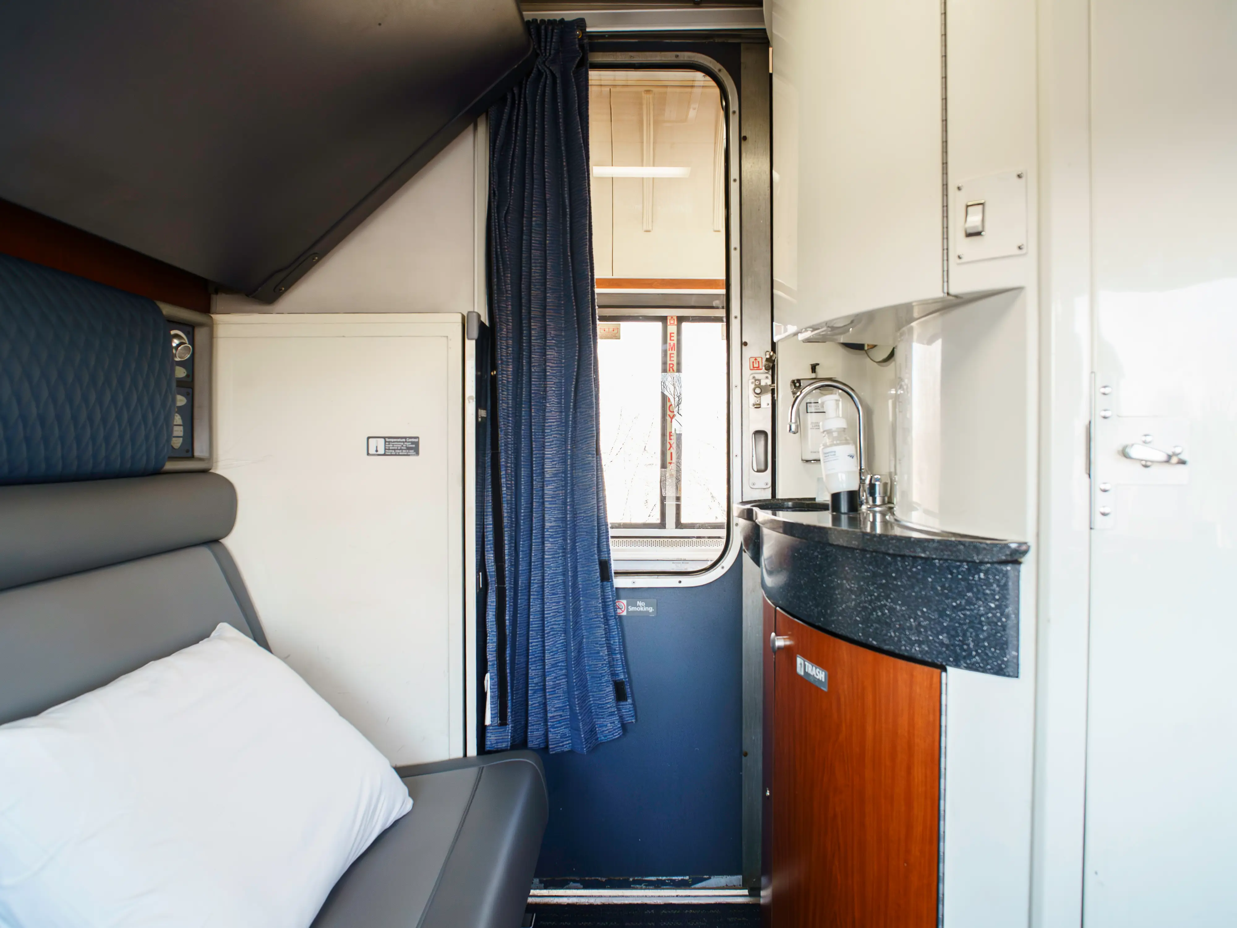 A bedroom on an Amtrak train with a seat on the left, a sink on the right, and a sliding door in the middle