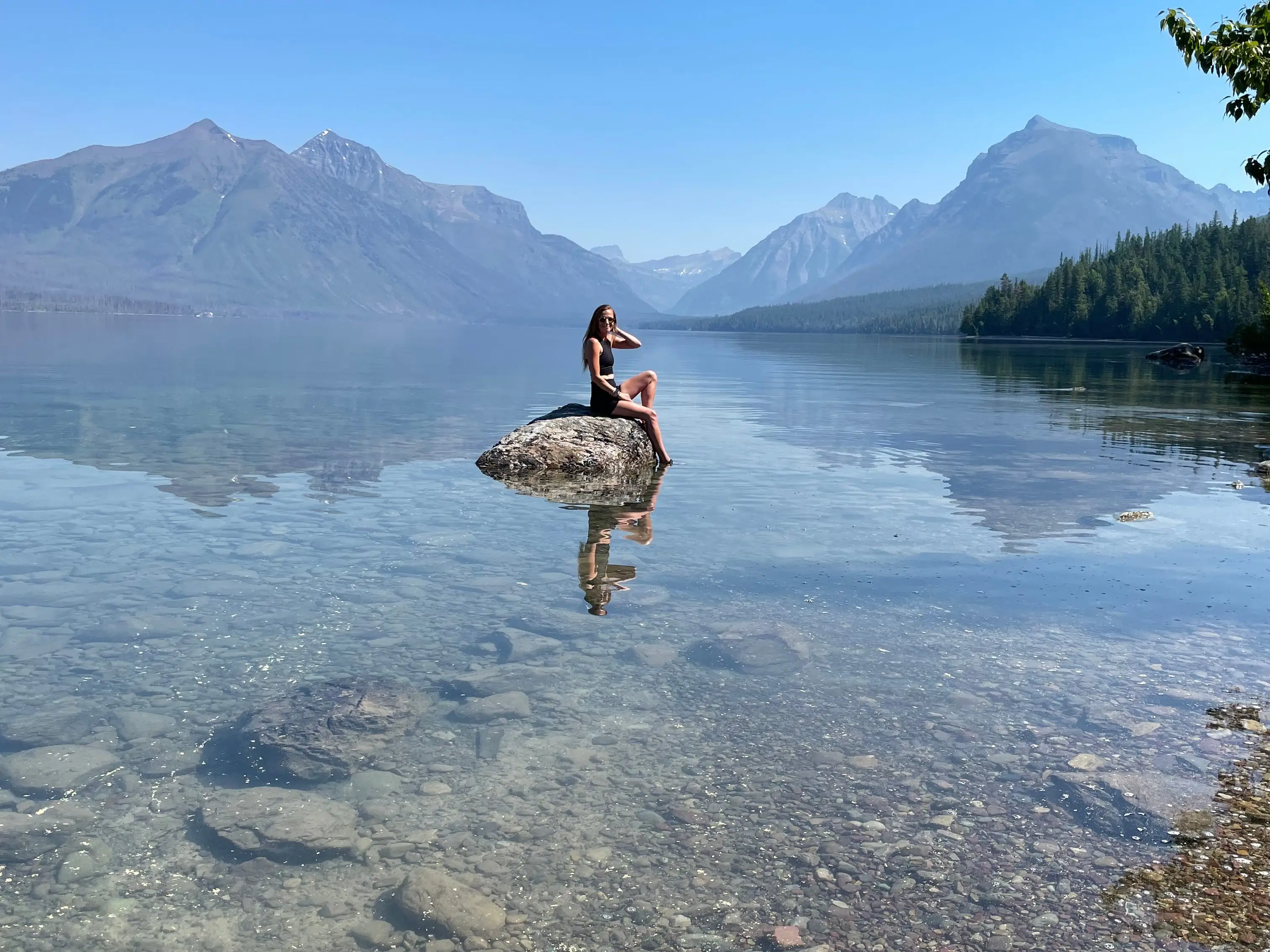 Emily sits on a rock in the middle of a lake that's surrounded by mountains.