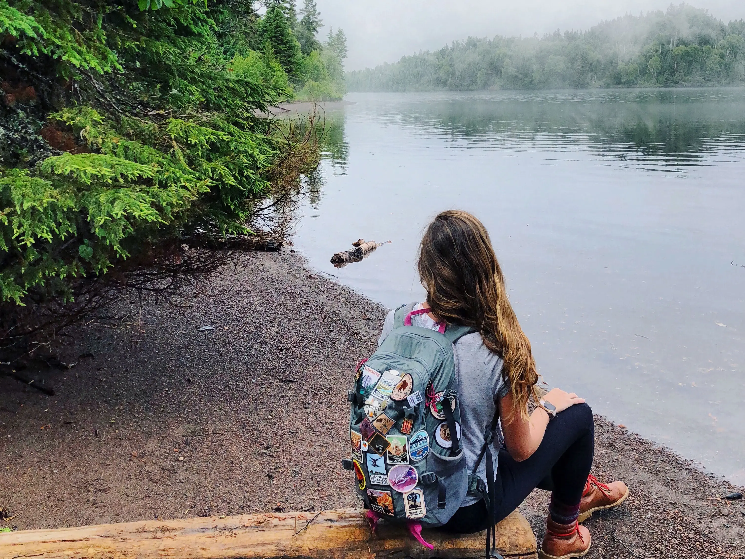 Emily sits on a log near the tree-lined shore of Isle Royale National Park.