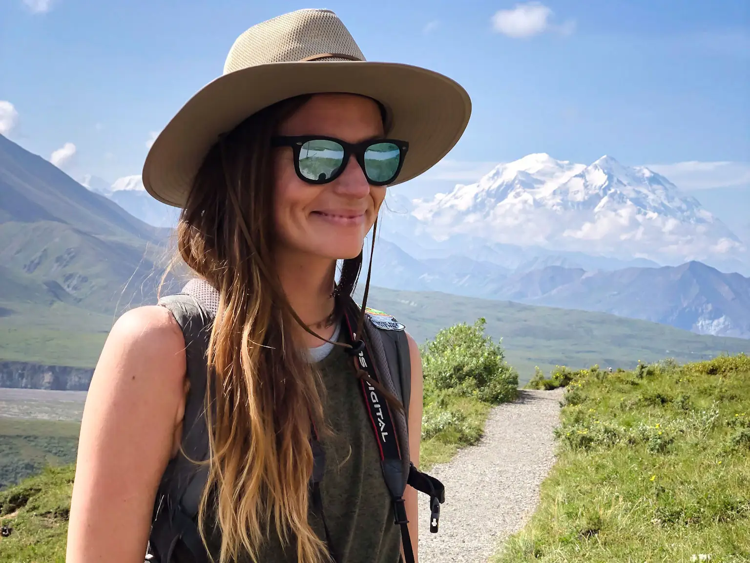 A photo of Emily, wearing a hat and sunglasses, with mountains behind her.