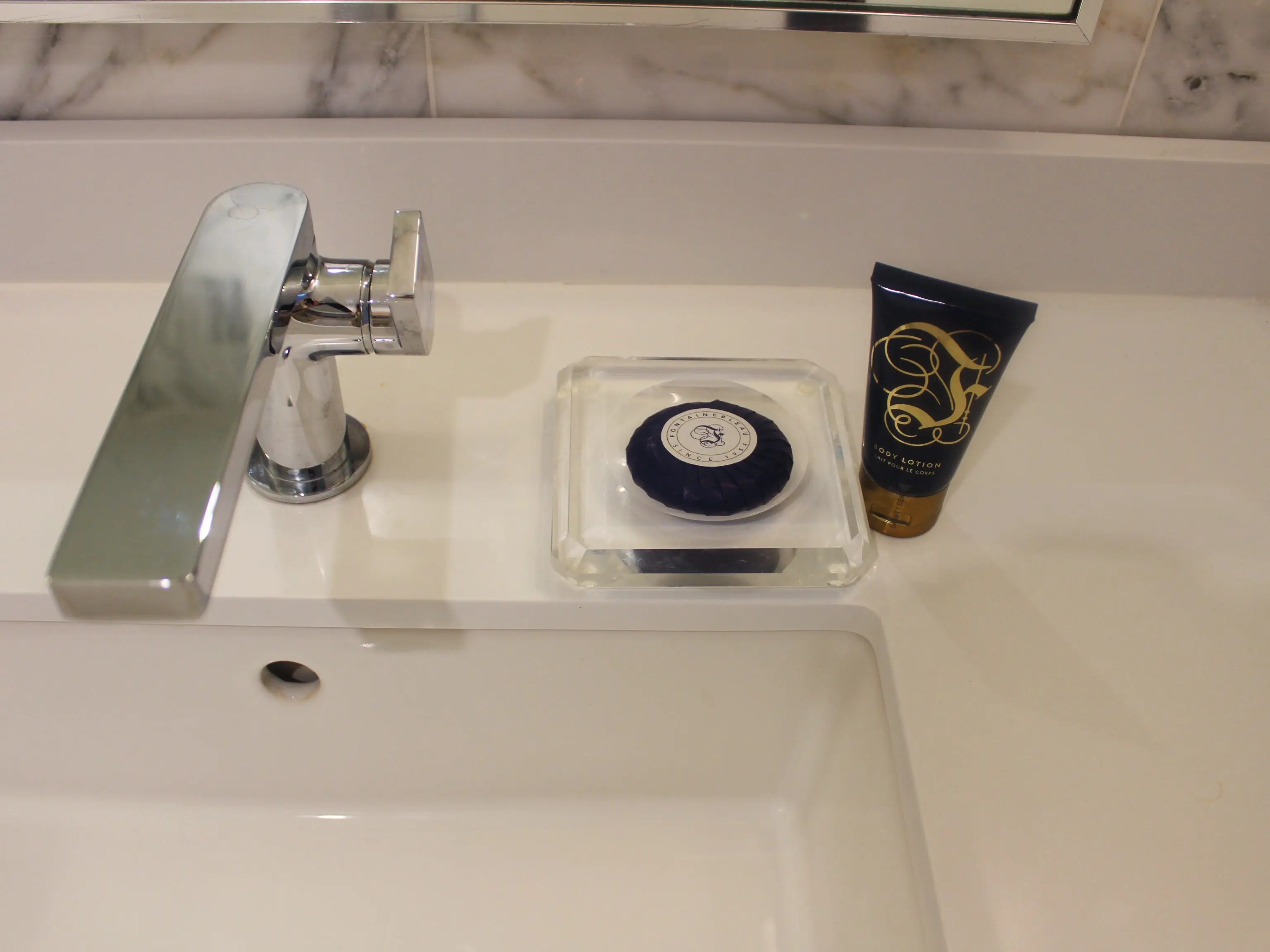 Bathroom sink counter with chrome faucet, soap dish, round bar soap, and a small toiletry tube.