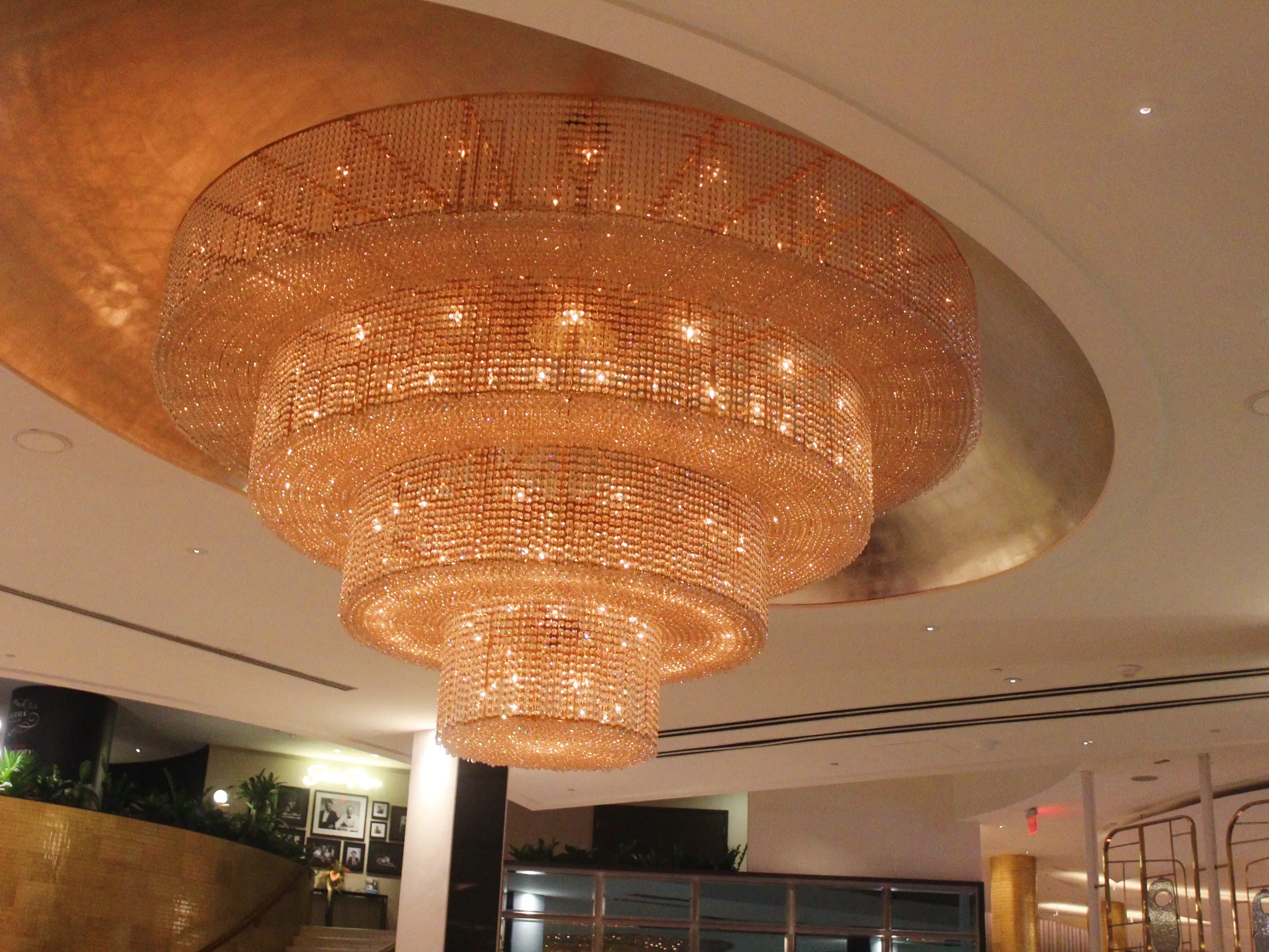 Large tiered crystal chandelier glows beneath a circular ceiling feature in an upscale interior lobby.