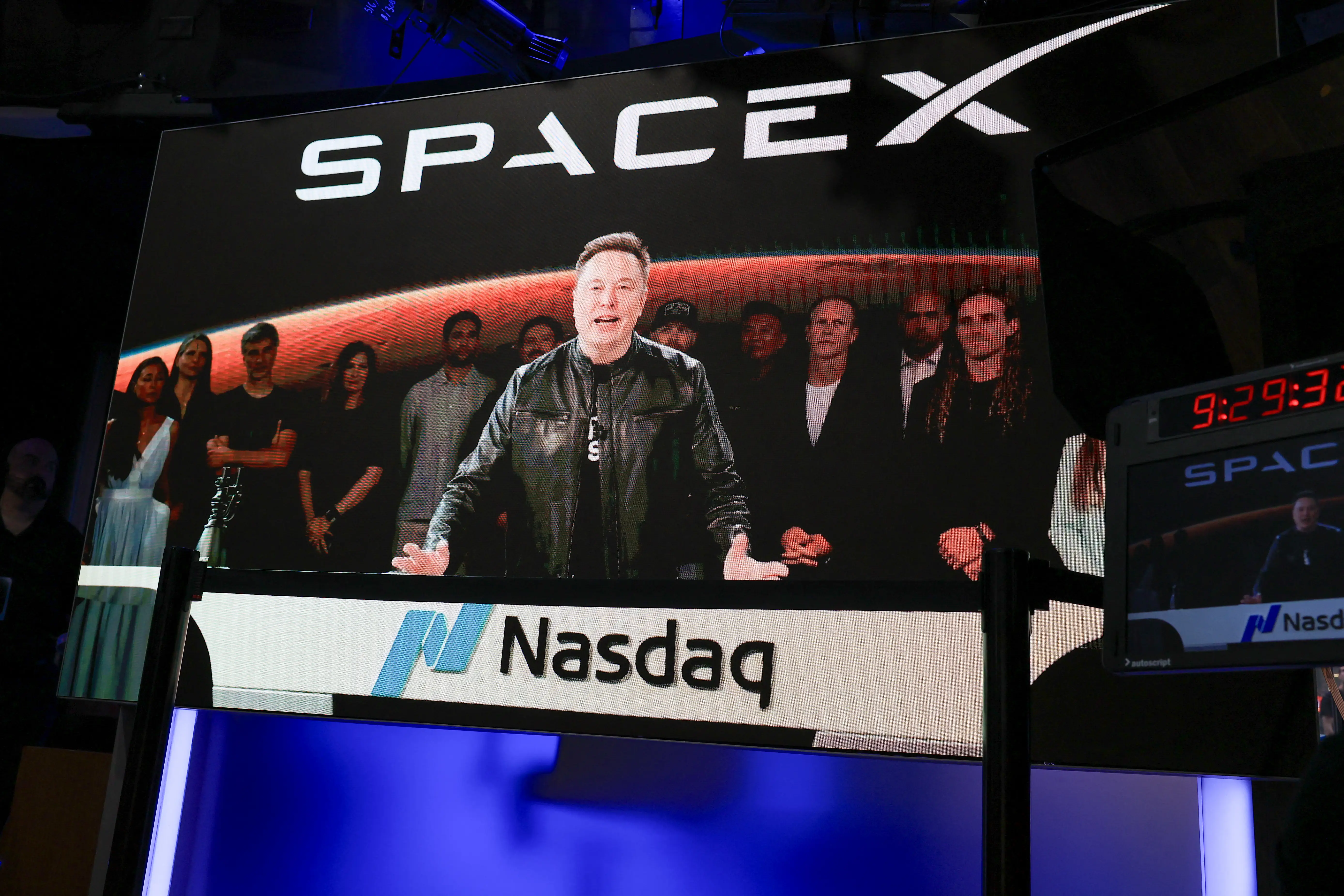 Elon Musk on a screen speaking virtually about the SpaceX IPO on the Nasdaq.
