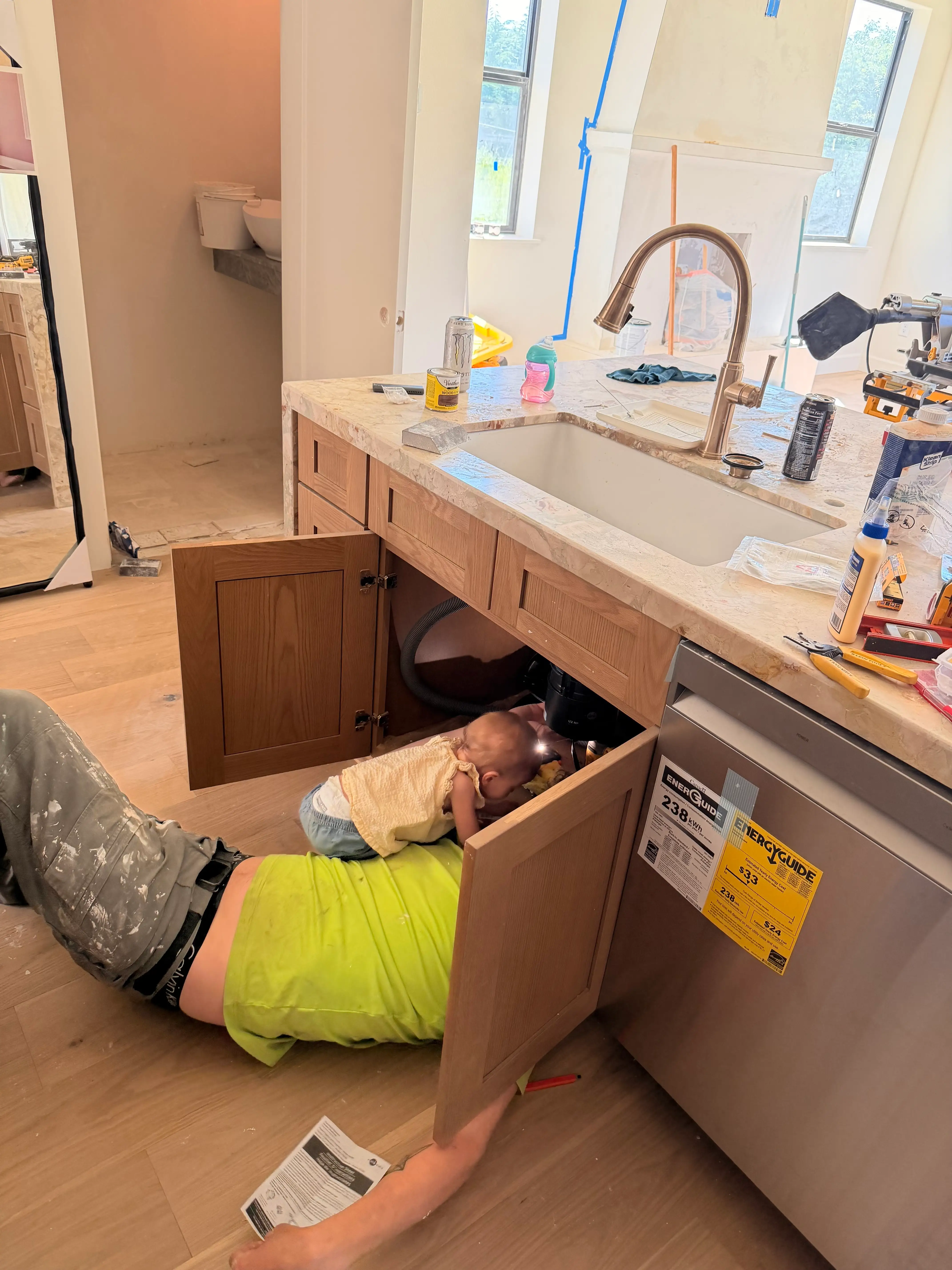 A man works on the piping under his sink as his daughter looks on.