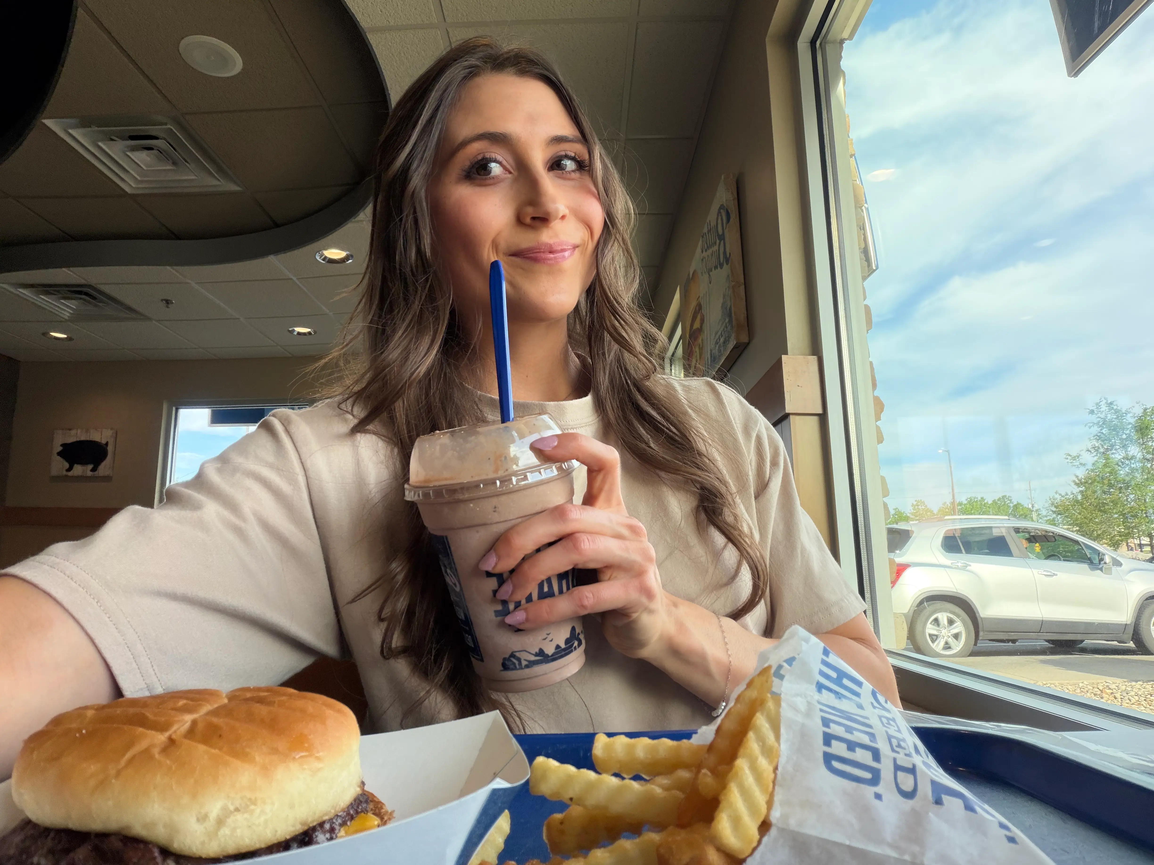 Woman smiling with Culver's concrete and tray of food in front of her in a Culver's