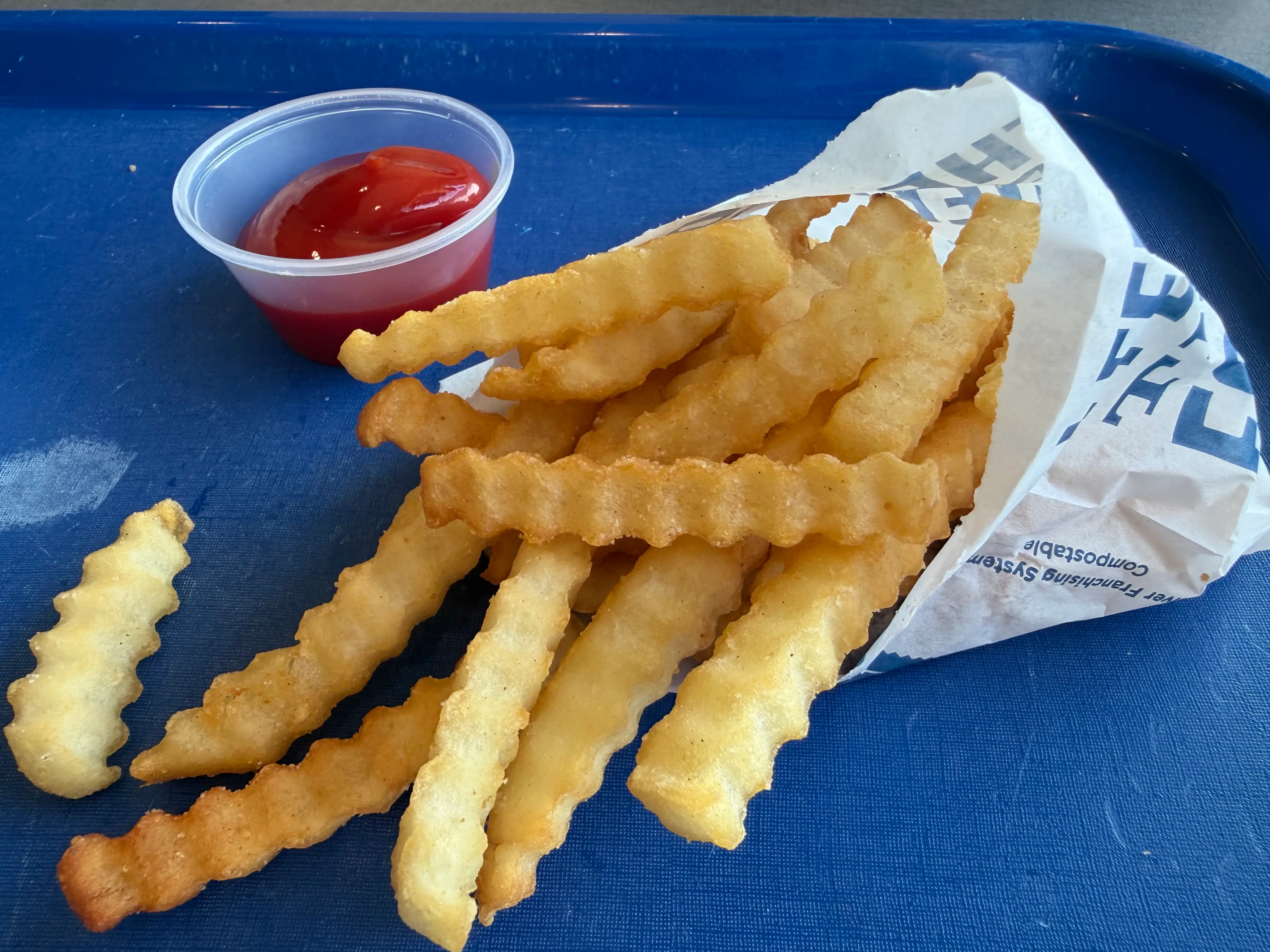 Crinkled fries in bag at Culver's next to container of ketchup