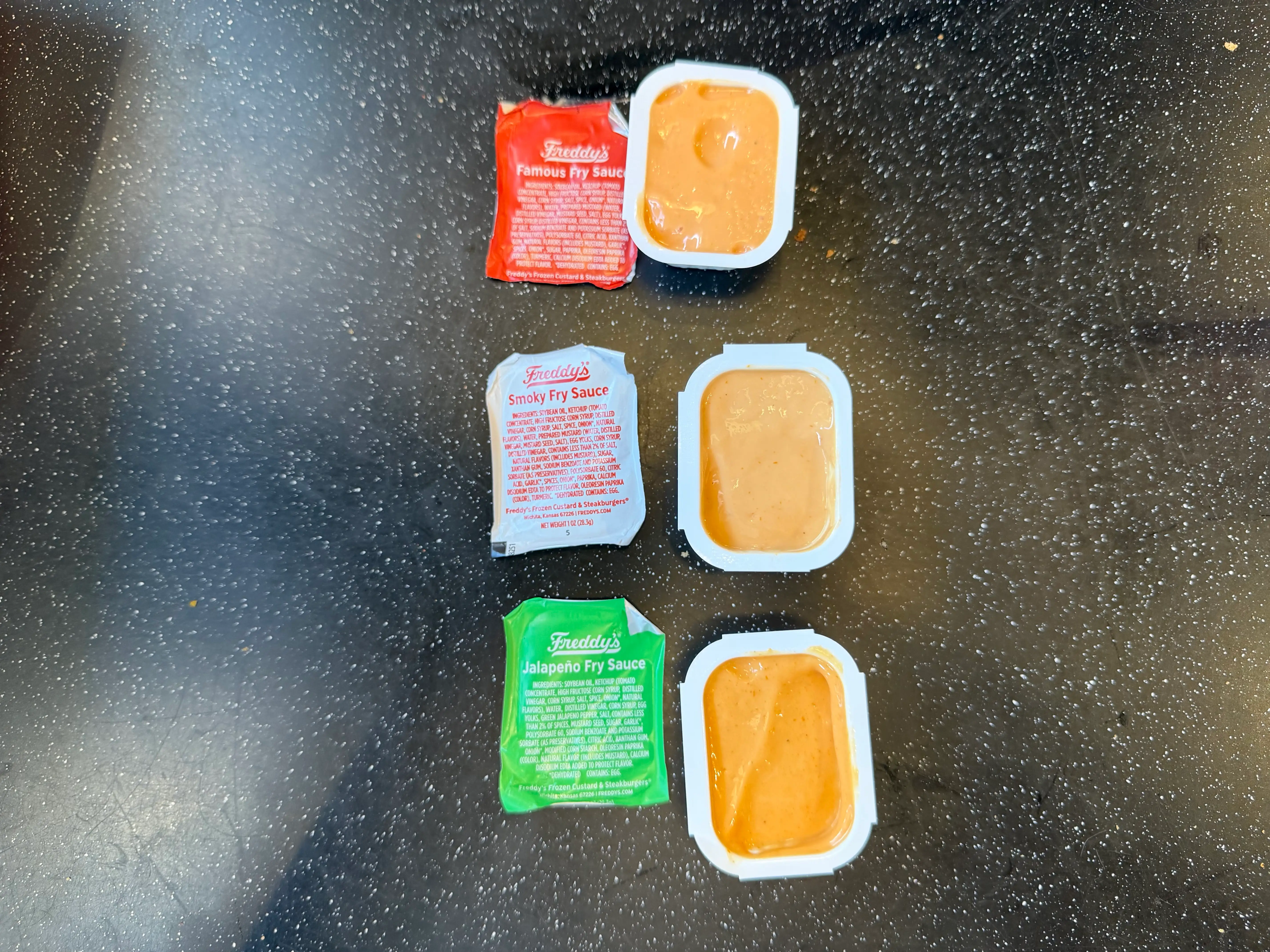 Freddy's famous fry sauce, Freddys smoky fry sauce, and Freddys jalapeno fry sauce containers, opened, with respective wrappers next to each
