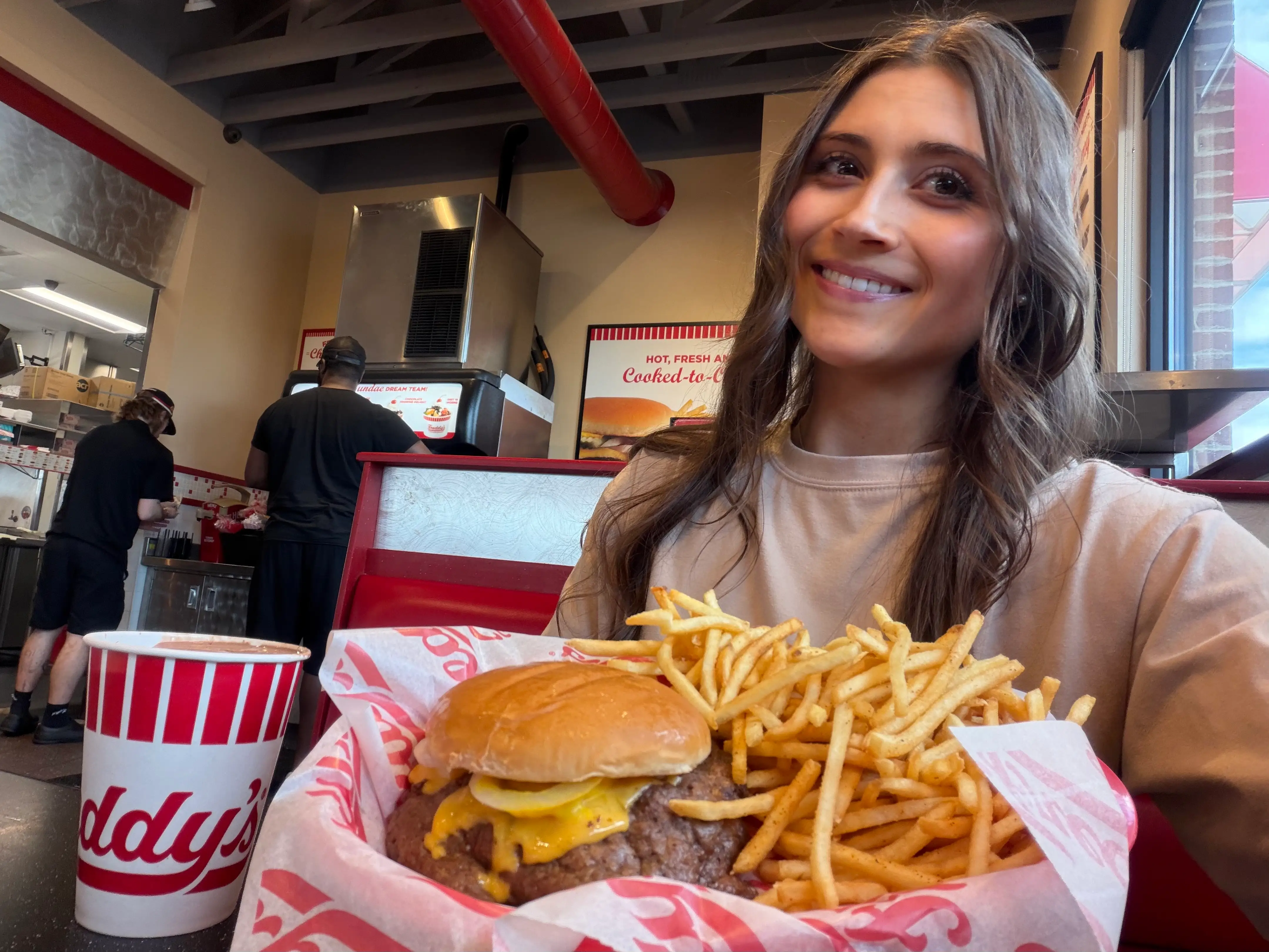 Woman smiling inside of a Freddy's with concrete, burger, fries