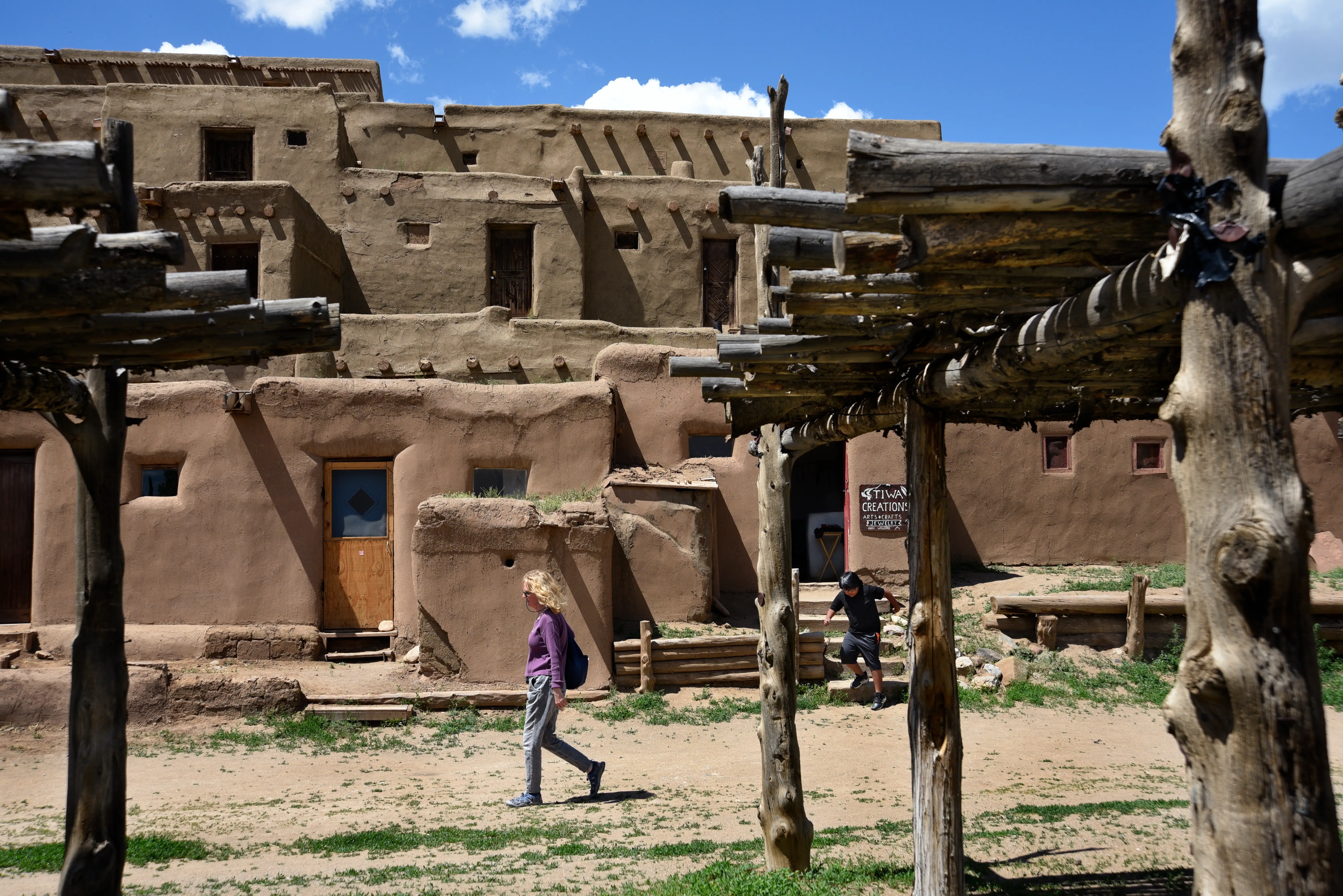 MAY 15, 2019: A tourist walks past the multi-story adobe residential complex at Taos Pueblo in Taos, New Mexico. The pueblo has been home to Native-Americans for more than one thousand years.