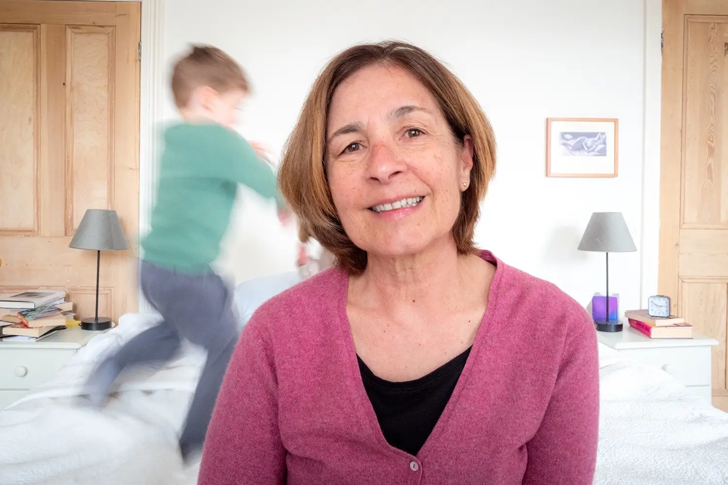 The author sitting on a bed with her grandchild playing in the bacground.