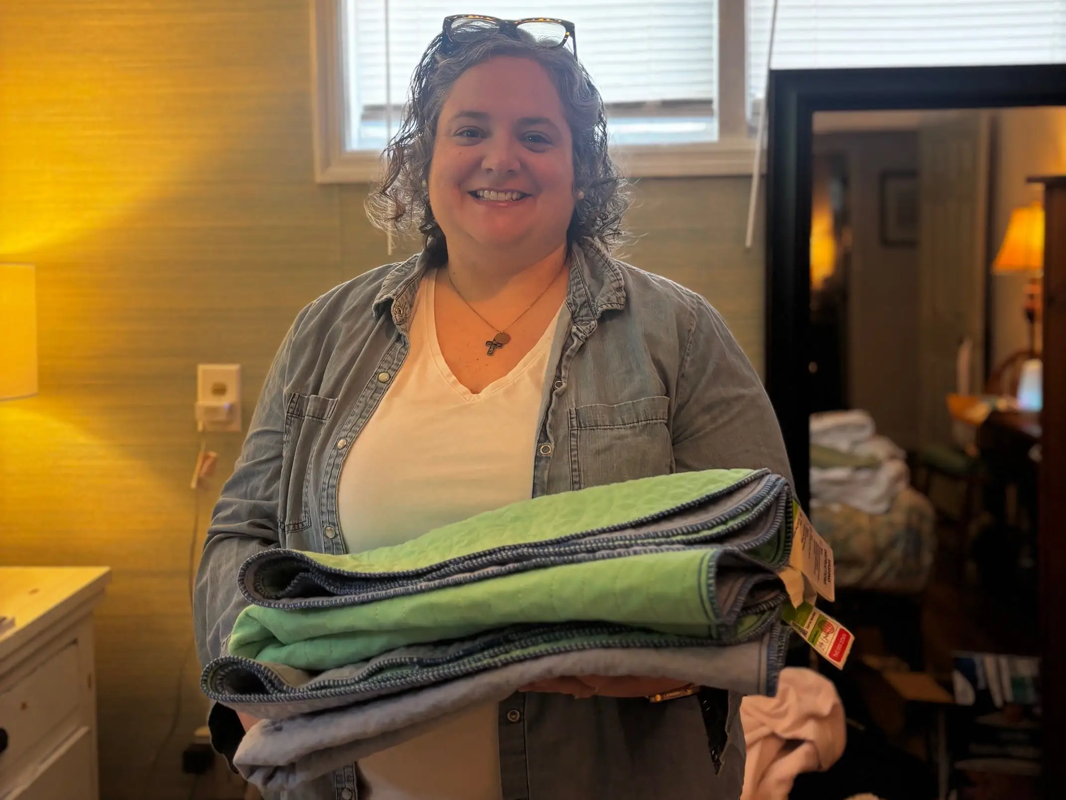 A woman holding a pile of towels in a bedroom.