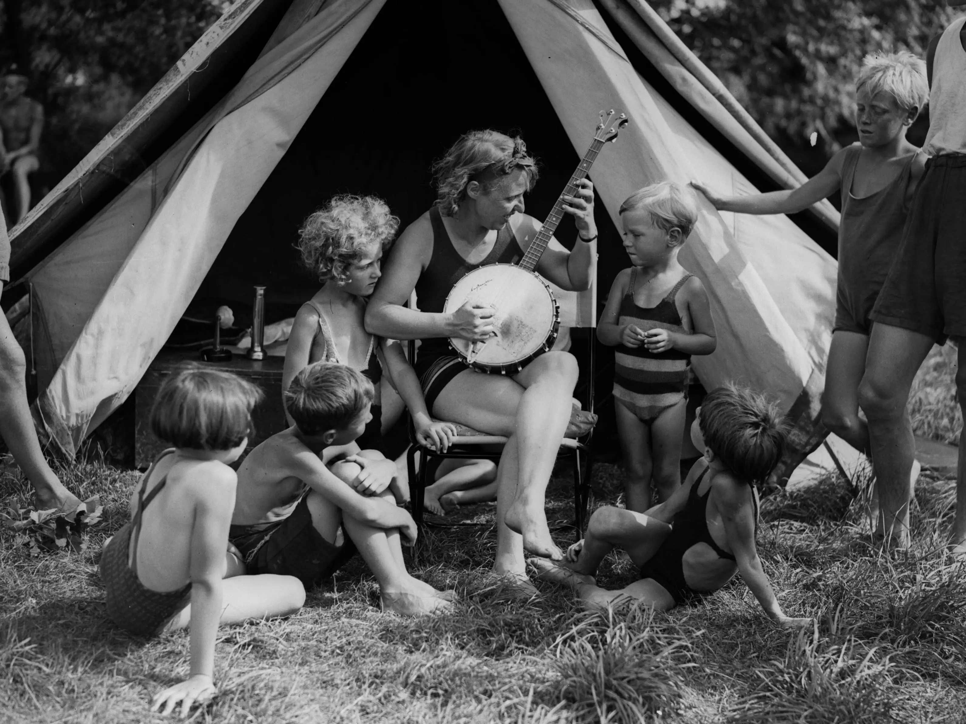 12th August 1933: Campers listen to some banjo music on the upper reaches of the River Thames.