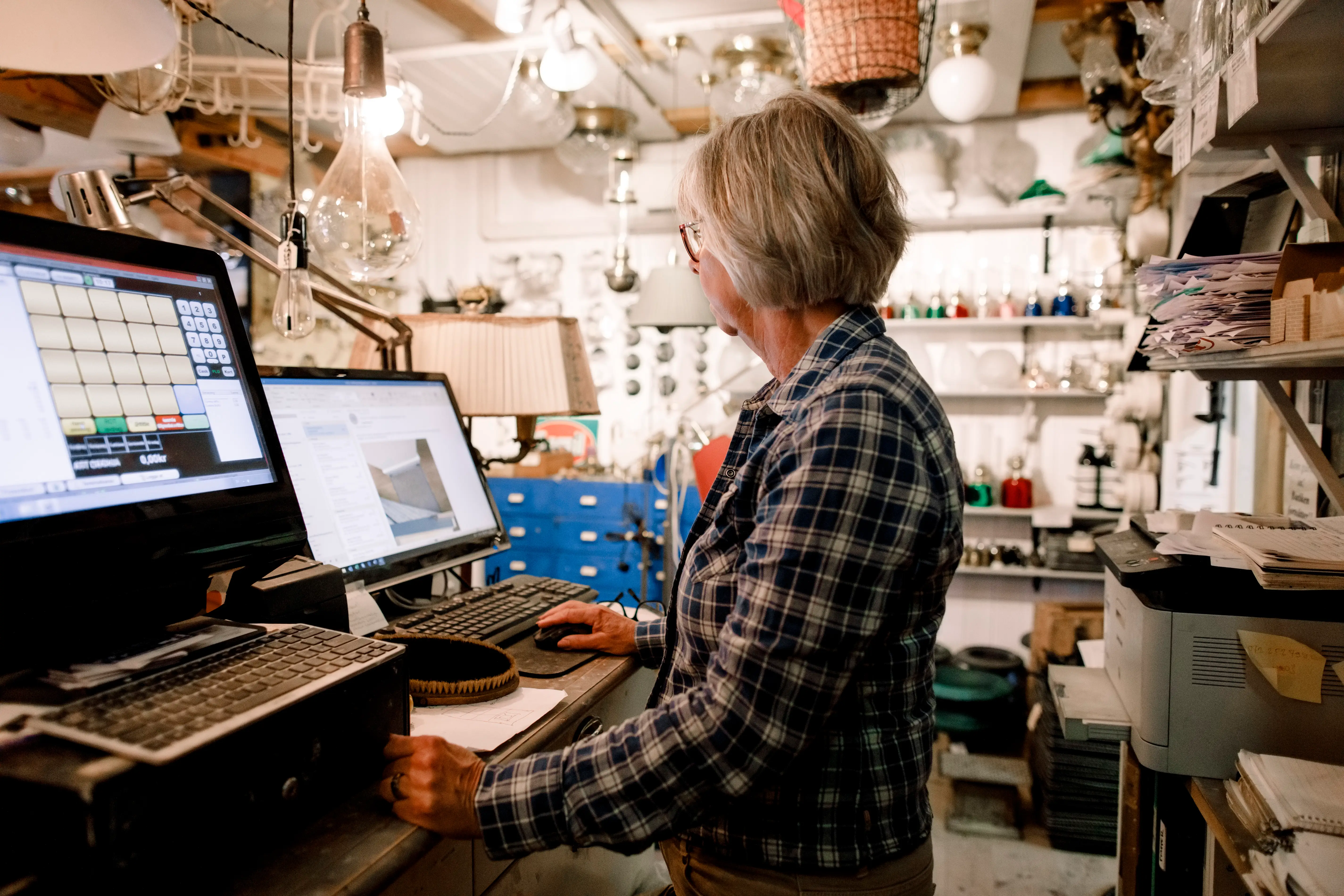 Side view of senior saleswoman using computer while standing at checkout in hardware store - stock photo