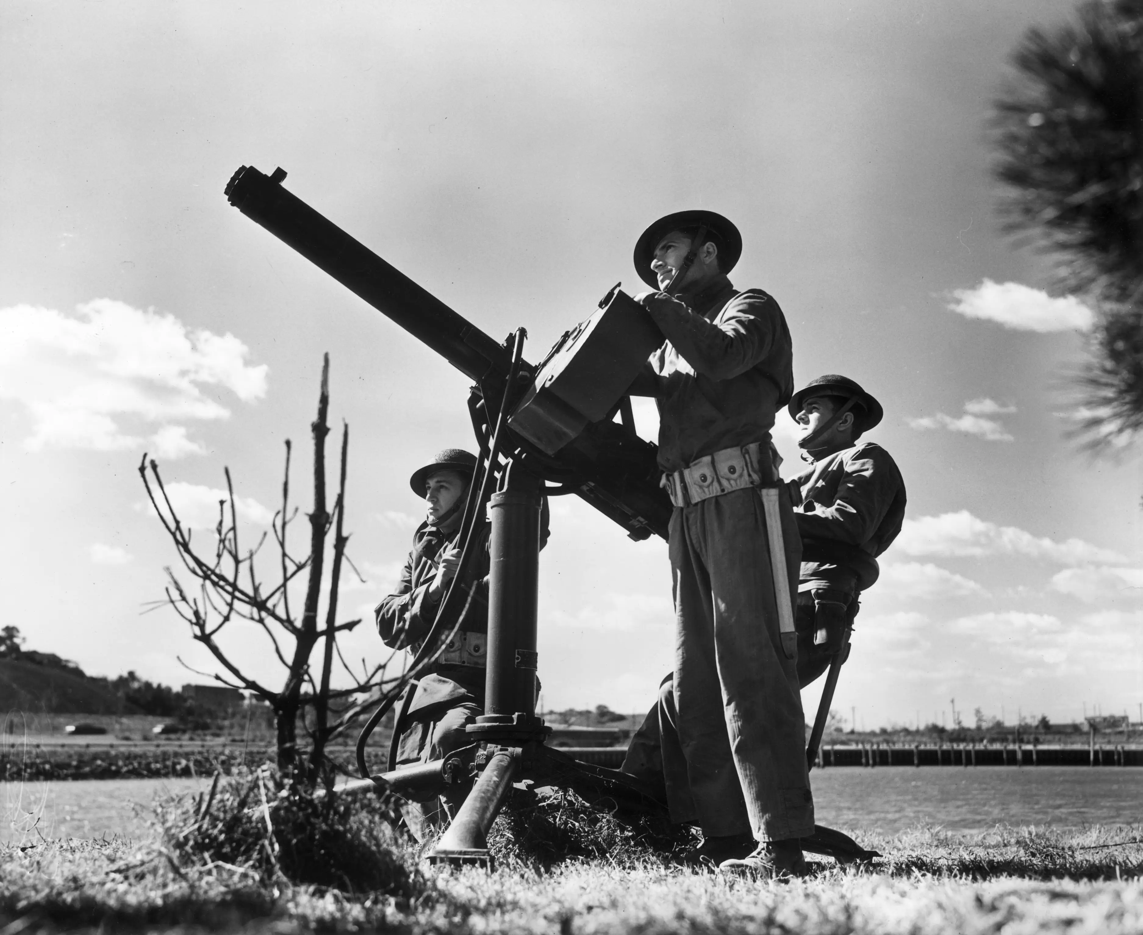 Three men beside a large mounted machine gun in a field in a black and white image