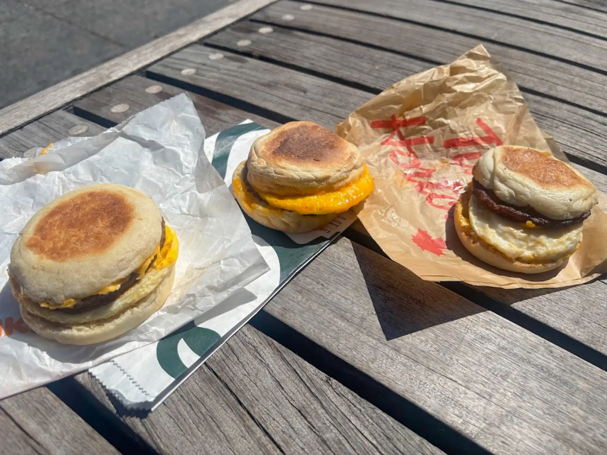 Three sausage, egg, and cheese sandwiches on a wooden table.