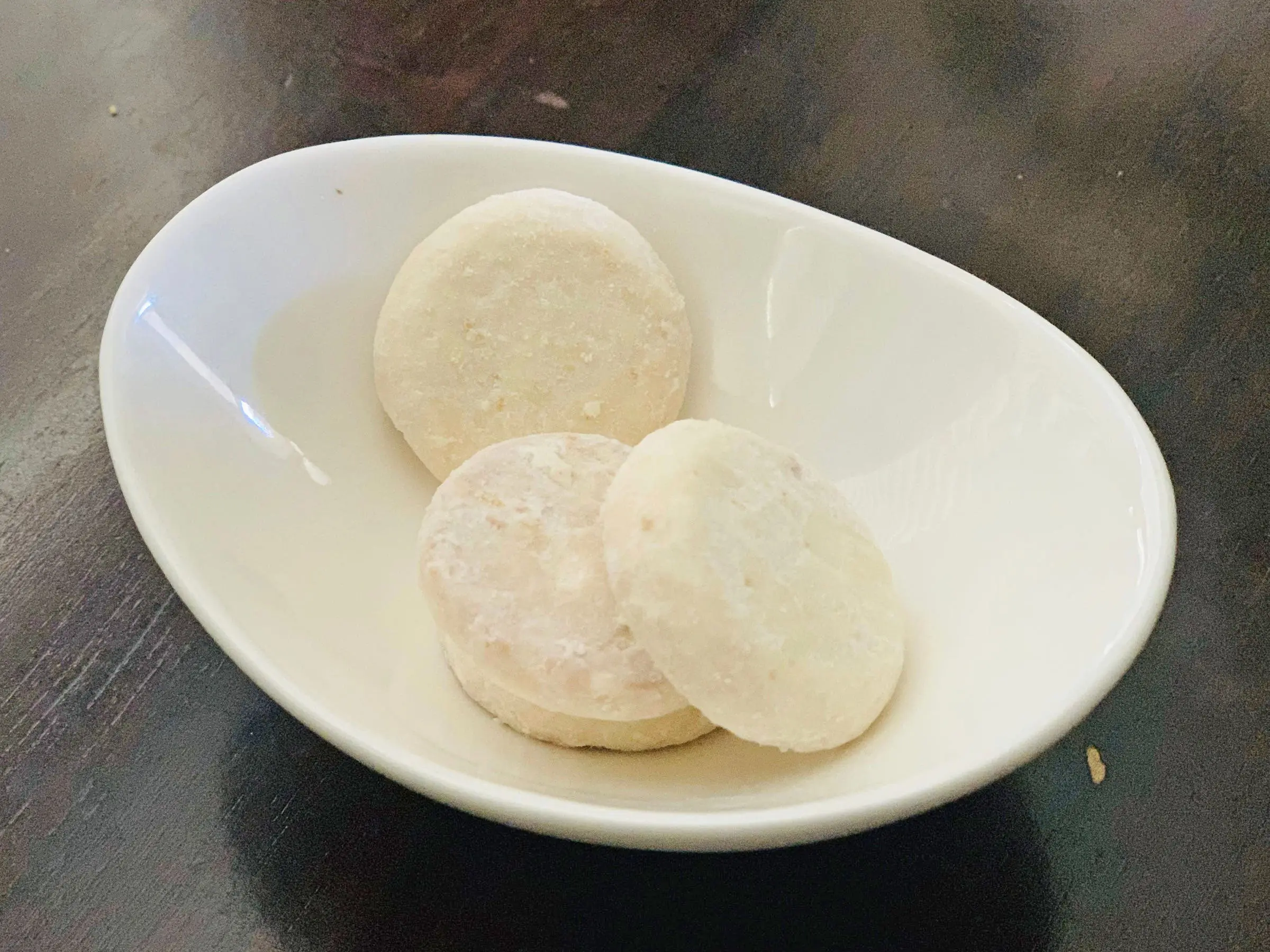 Three Trader Joe's key-lime tea cookies in a small white bowl on a dark wood table.