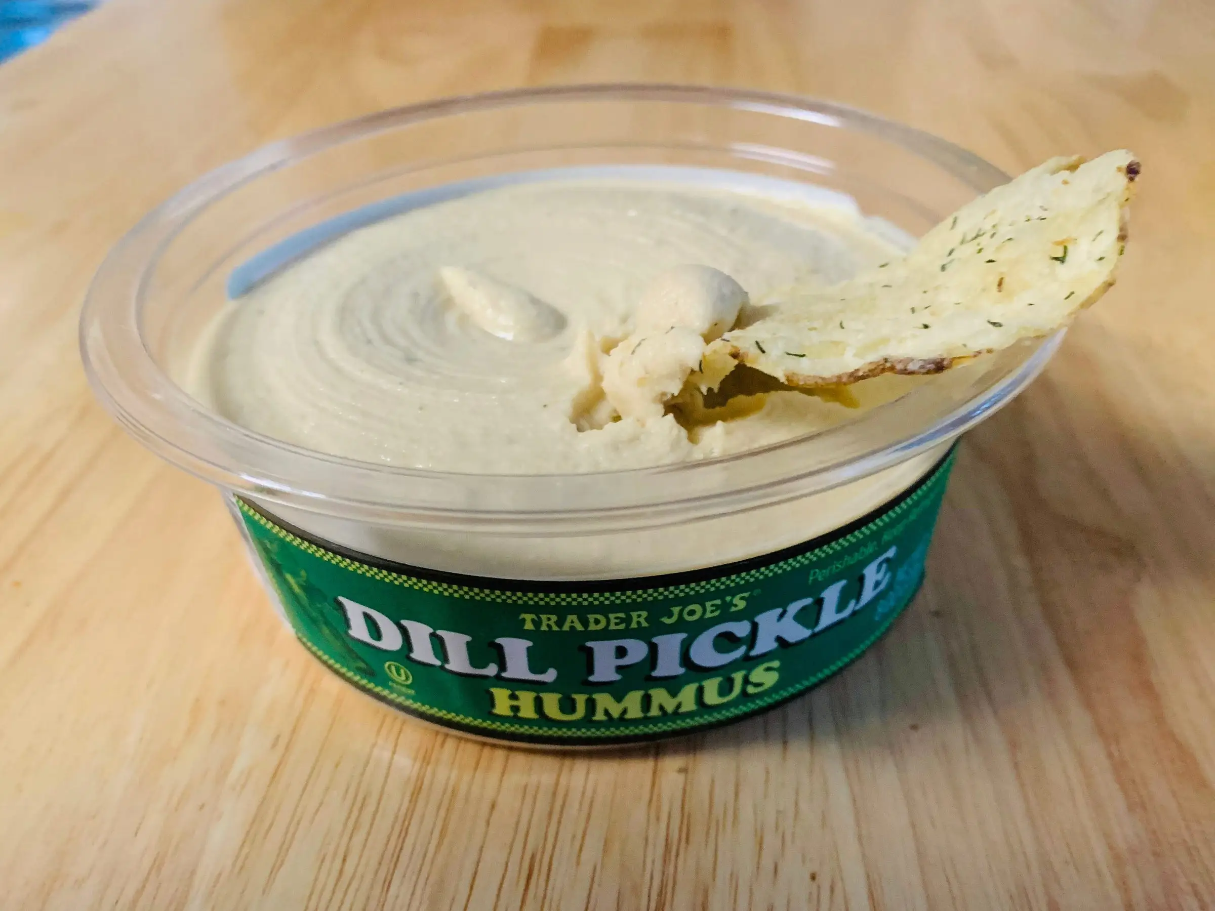 A chip in an open container of Trader Joe's dill-pickle hummus.